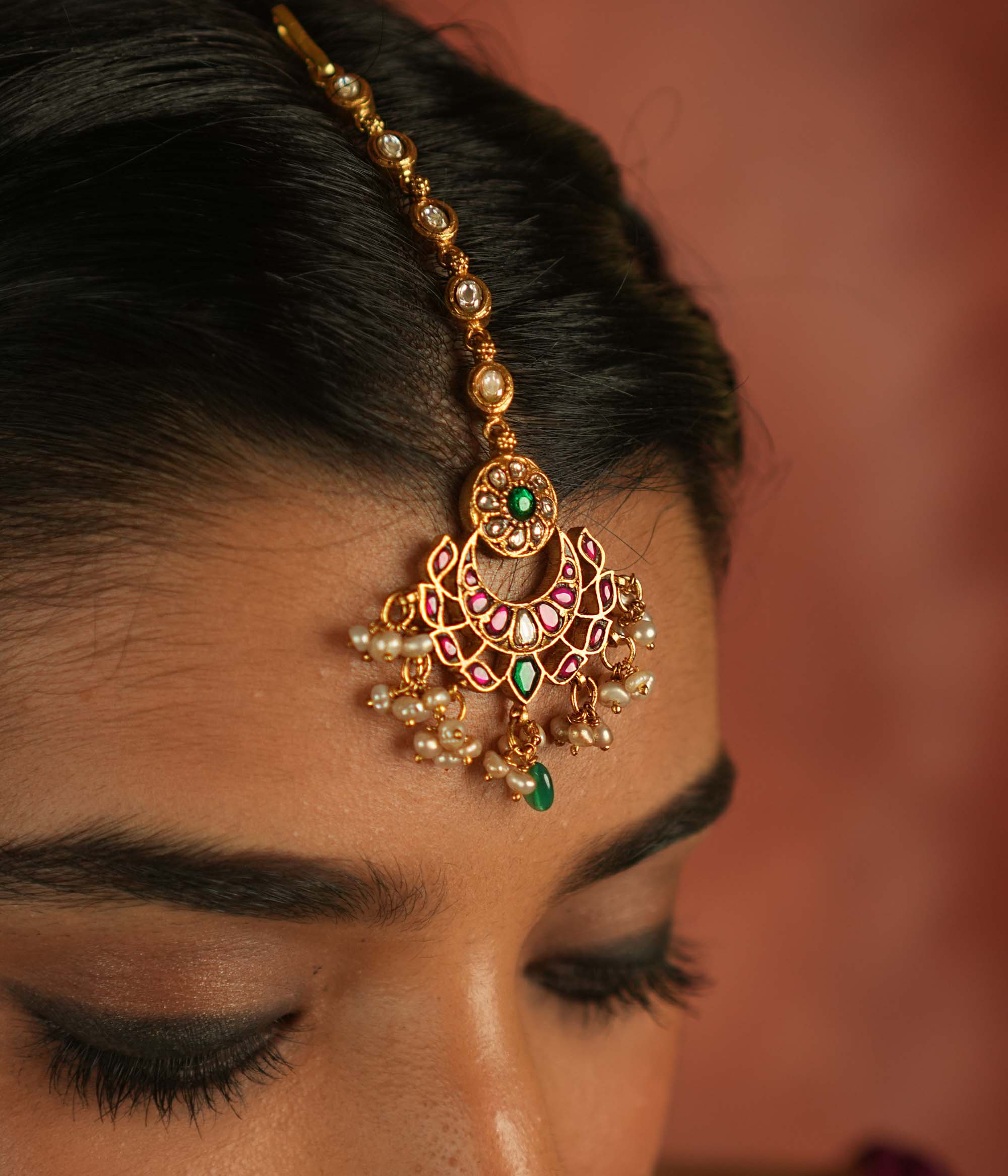 Ethereal elegance! This floral maangtika, adorned with Polki stones and red, green, and white Kundan gems, shimmers with pearls and green beads—whispering celestial charm and timeless grace.