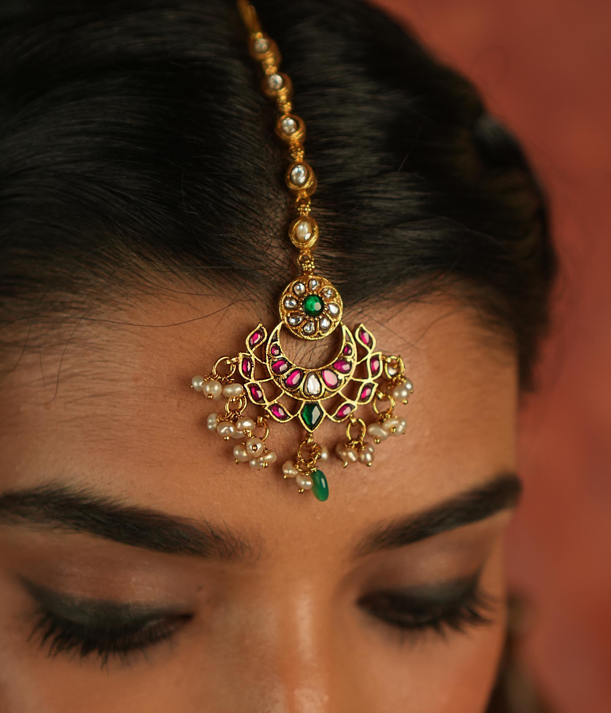 Ethereal elegance! This floral maangtika, adorned with Polki stones and red, green, and white Kundan gems, shimmers with pearls and green beads—whispering celestial charm and timeless grace.