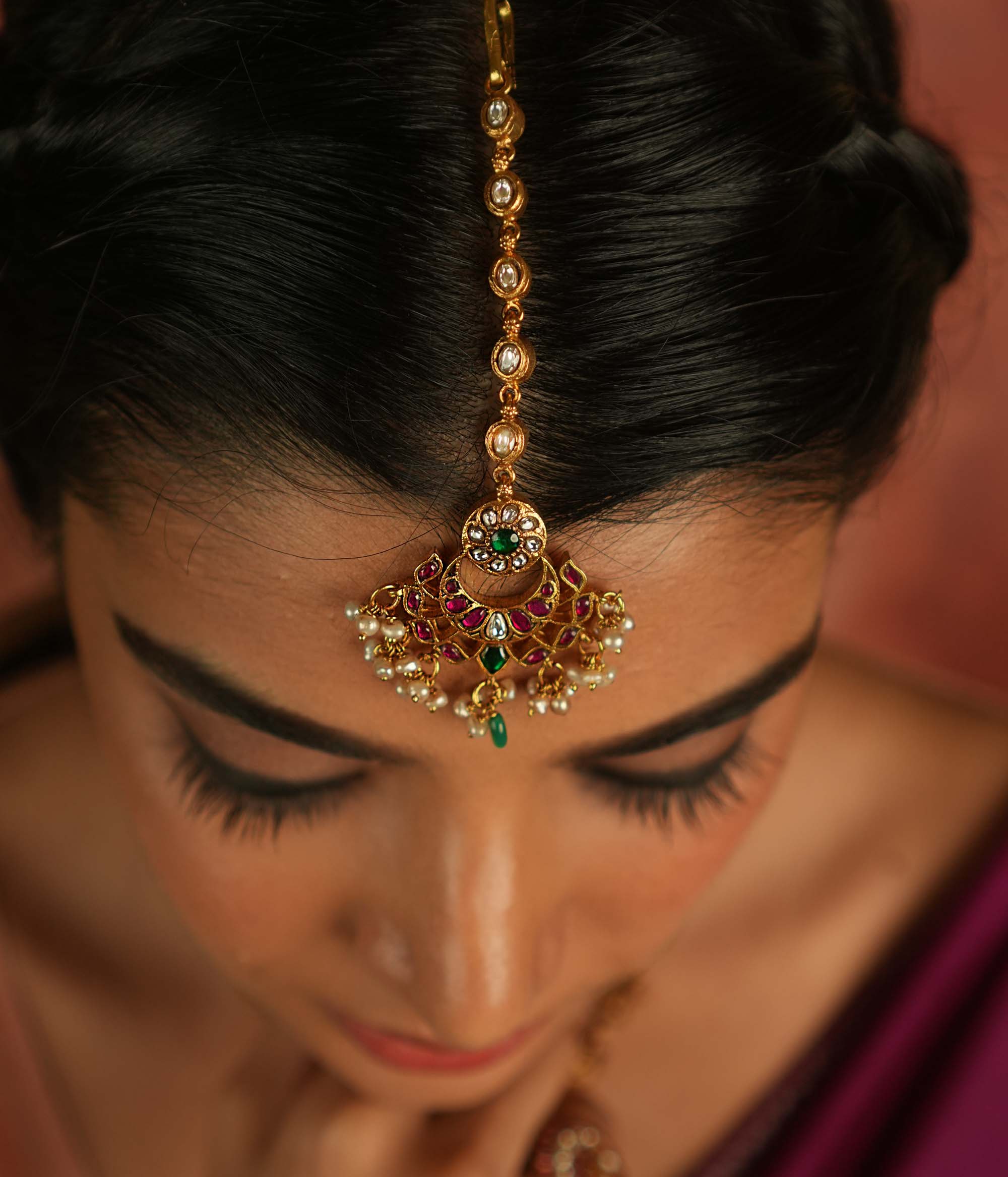 Ethereal elegance! This floral maangtika, adorned with Polki stones and red, green, and white Kundan gems, shimmers with pearls and green beads—whispering celestial charm and timeless grace.