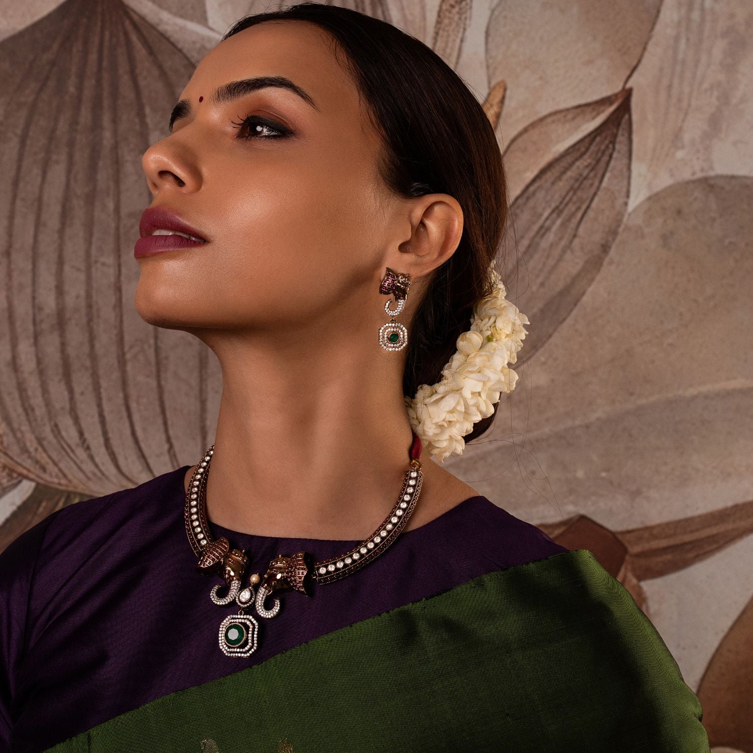Gold-plated silver earring featuring an intricately designed elephant-shaped stud. The elephant's ears are adorned with vibrant red cut stones, while its trunk sparkles with CZ stones. A stunning green cut stone drop hangs below, encircled by shimmering CZ stones, adding elegance and charm to this unique design.