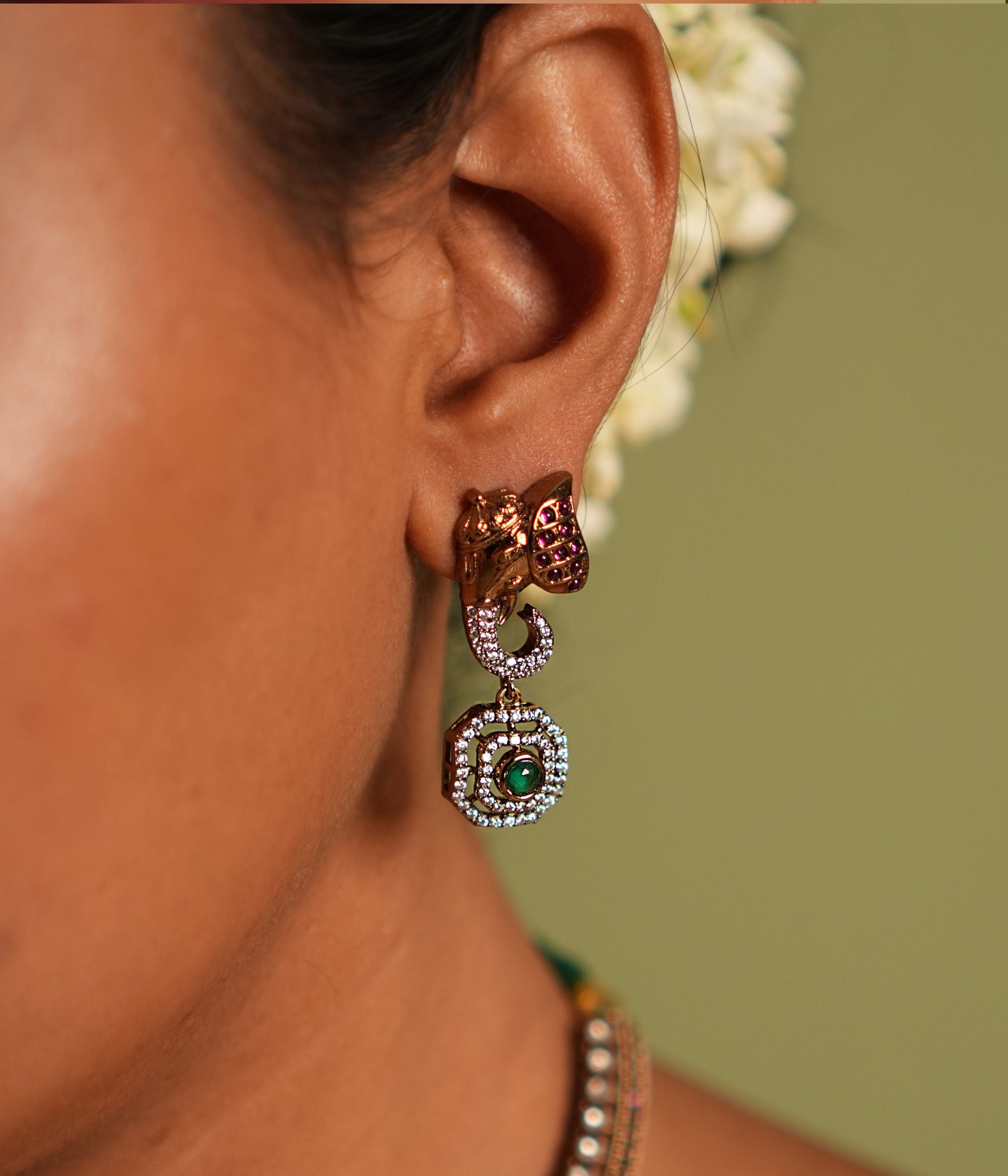 Gold-plated silver earring featuring an intricately designed elephant-shaped stud. The elephant's ears are adorned with vibrant red cut stones, while its trunk sparkles with CZ stones. A stunning green cut stone drop hangs below, encircled by shimmering CZ stones, adding elegance and charm to this unique design.