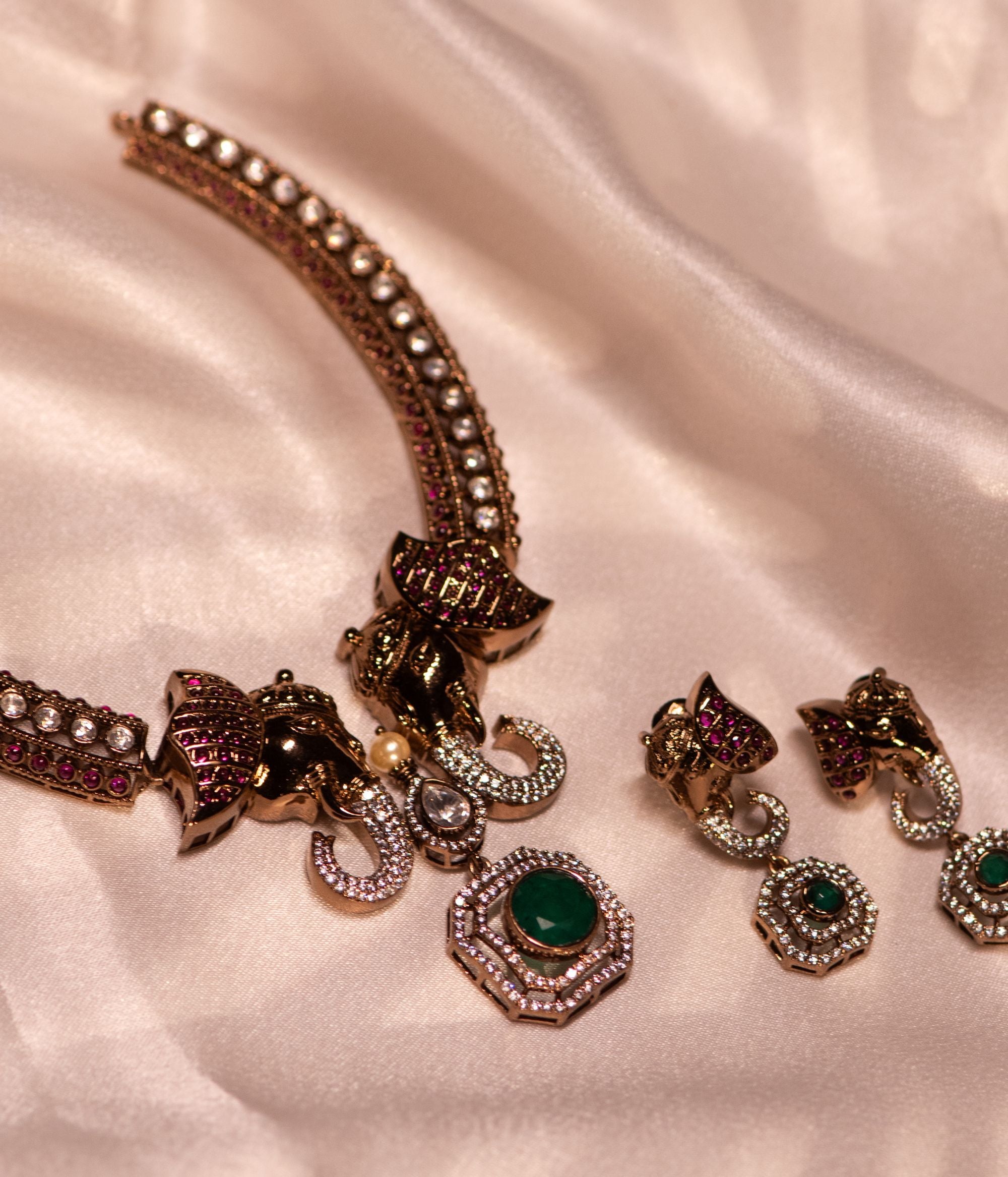 Gold-plated silver earring featuring an intricately designed elephant-shaped stud. The elephant's ears are adorned with vibrant red cut stones, while its trunk sparkles with CZ stones. A stunning green cut stone drop hangs below, encircled by shimmering CZ stones, adding elegance and charm to this unique design.