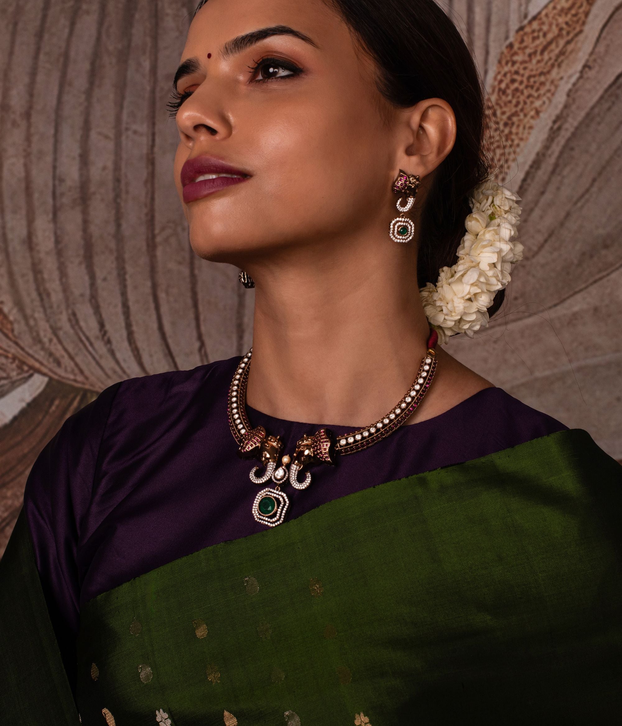 Gold-plated silver earring featuring an intricately designed elephant-shaped stud. The elephant's ears are adorned with vibrant red cut stones, while its trunk sparkles with CZ stones. A stunning green cut stone drop hangs below, encircled by shimmering CZ stones, adding elegance and charm to this unique design.