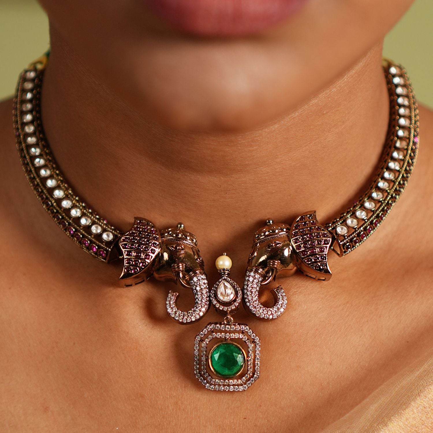 "Gold-plated silver Kanti necklace featuring an intricately designed elephant-shaped pendant. The elephant's ears are adorned with vibrant red cut stones, while its trunk is embellished with shimmering CZ stones. A striking green cut stone drop, encircled by CZ stones, adds an elegant finish to the design, making this necklace a perfect blend of tradition and sophistication.