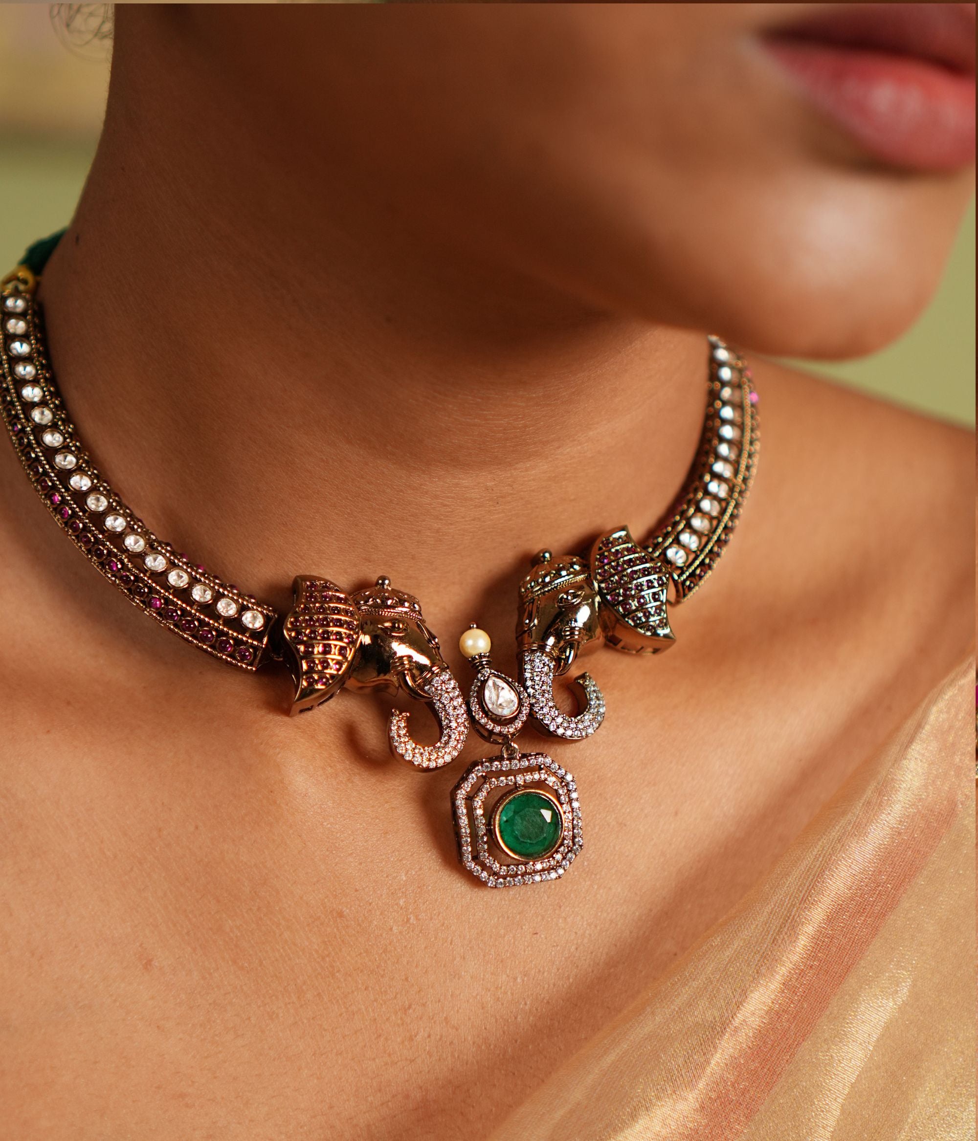 "Gold-plated silver Kanti necklace featuring an intricately designed elephant-shaped pendant. The elephant's ears are adorned with vibrant red cut stones, while its trunk is embellished with shimmering CZ stones. A striking green cut stone drop, encircled by CZ stones, adds an elegant finish to the design, making this necklace a perfect blend of tradition and sophistication.
