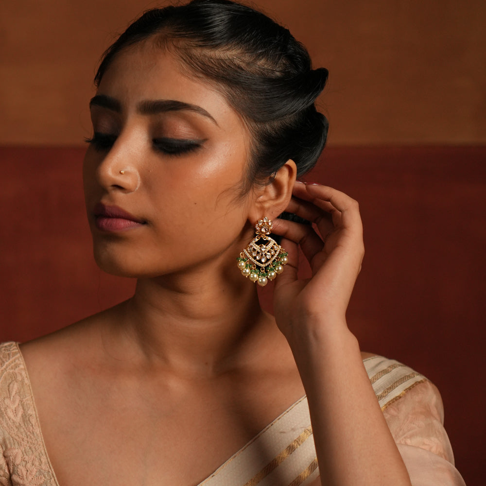 Exquisite gold-plated silver dangler earrings featuring a stunning floral design adorned with shimmering Polki and CZ stones. The elegant drops are embellished with delicate white pearls and vibrant green beads, adding a graceful and timeless charm. A perfect blend of tradition and elegance, these earrings are ideal for any occasion.