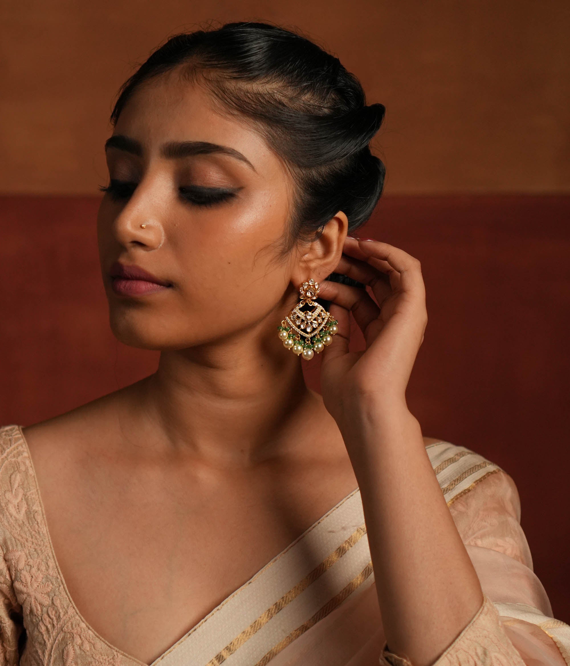 Exquisite gold-plated silver dangler earrings featuring a stunning floral design adorned with shimmering Polki and CZ stones. The elegant drops are embellished with delicate white pearls and vibrant green beads, adding a graceful and timeless charm. A perfect blend of tradition and elegance, these earrings are ideal for any occasion.