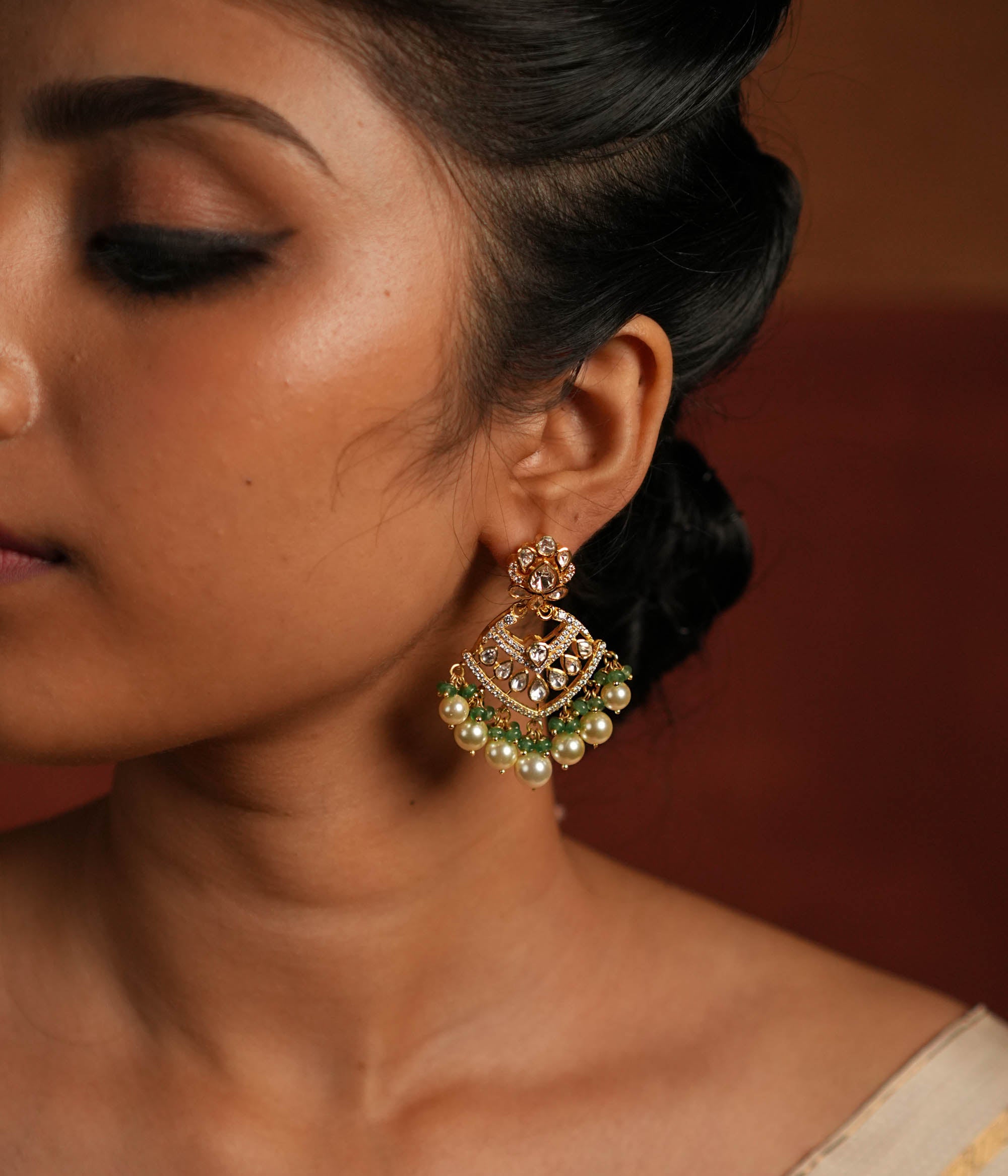 Exquisite gold-plated silver dangler earrings featuring a stunning floral design adorned with shimmering Polki and CZ stones. The elegant drops are embellished with delicate white pearls and vibrant green beads, adding a graceful and timeless charm. A perfect blend of tradition and elegance, these earrings are ideal for any occasion.