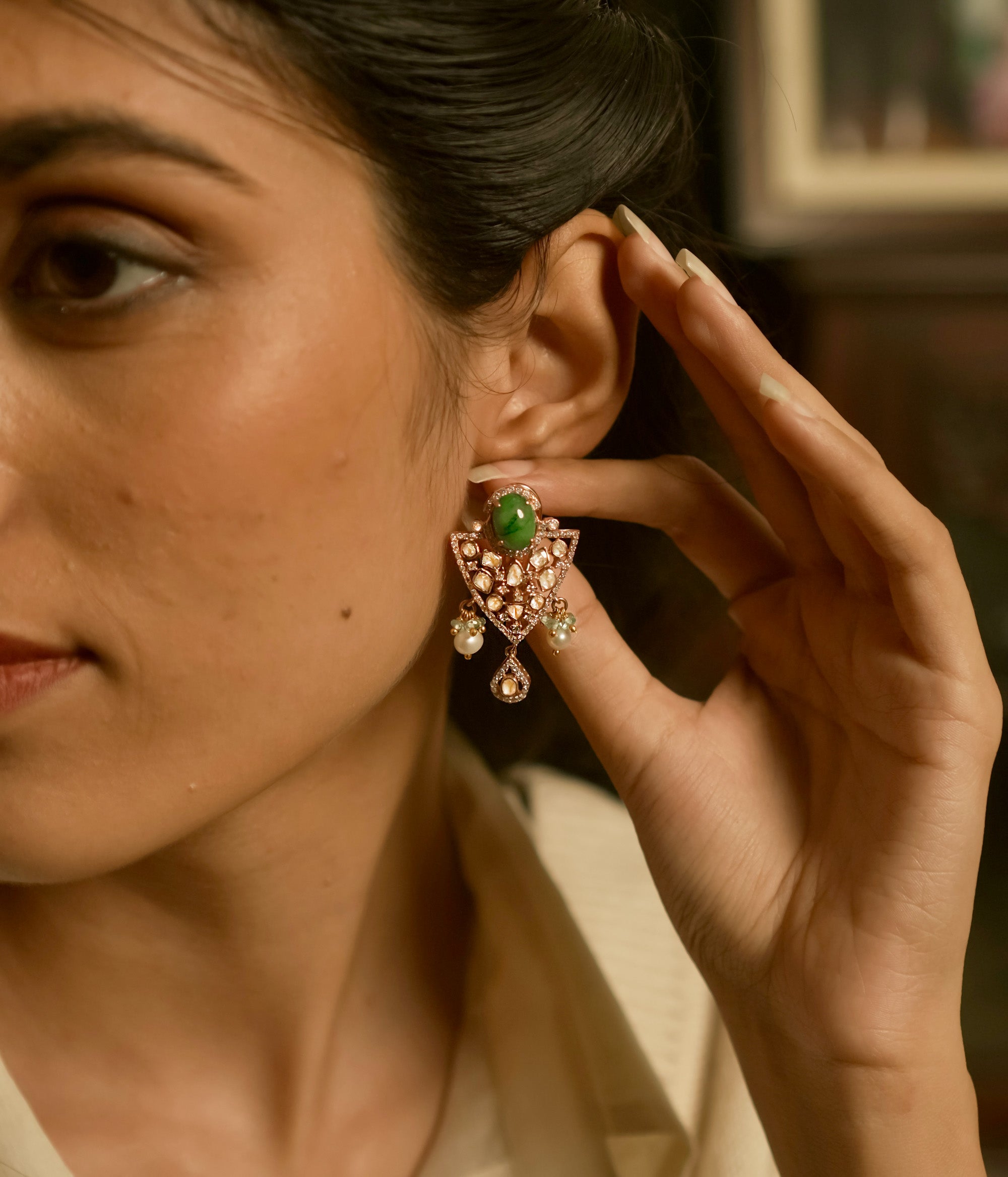 Triangular polki earrings with green gemstone, pearls, CZ accents, and tassel drop design.