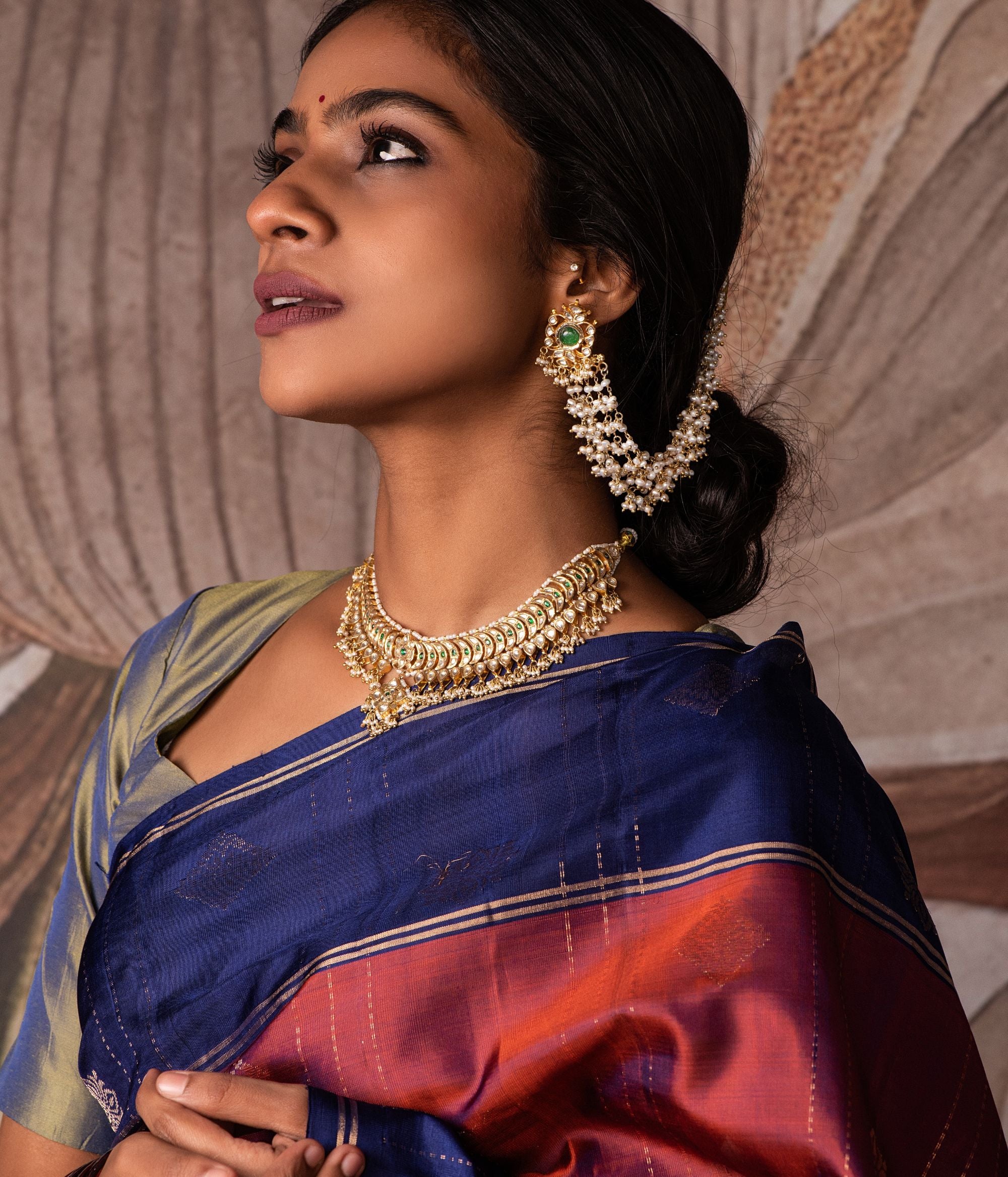 Gold-plated silver ear chain featuring a delicate string of Fresh Water Pearls, elegantly designed to connect to a hairpin at the end. The hairpin is adorned with Rubies, White Sapphires, and Emeralds, adding a regal touch. This exquisite piece enhances any traditional look with its graceful and sophisticated appeal.