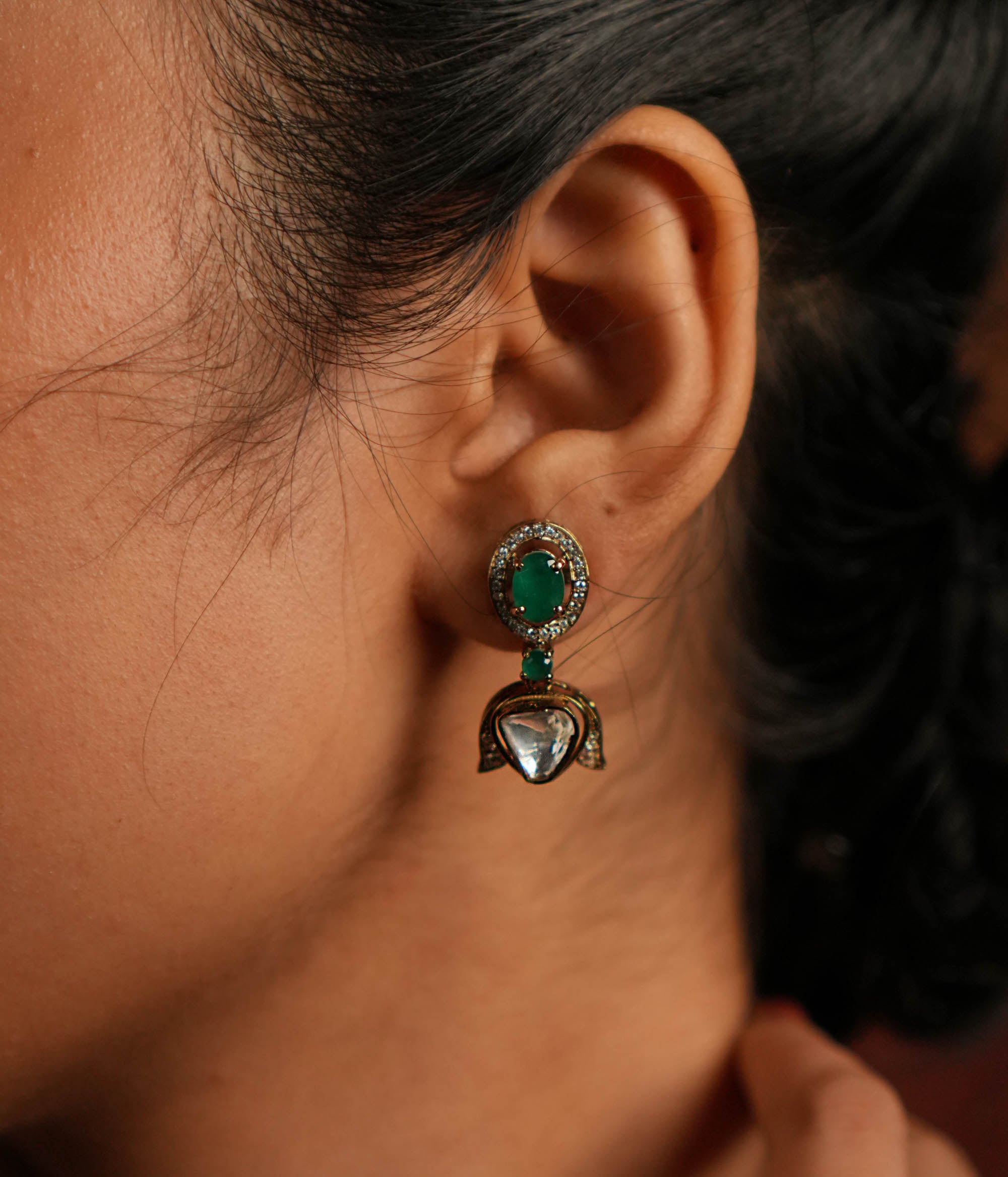 Elegant gold-plated silver drop earrings featuring a striking green spinel stone at the center, beautifully encased by shimmering CZ stones. The design is enhanced with a delicate Polki stone drop, also surrounded by CZ stones, adding a touch of timeless charm. A perfect blend of sophistication and elegance, making it an exquisite statement accessory.