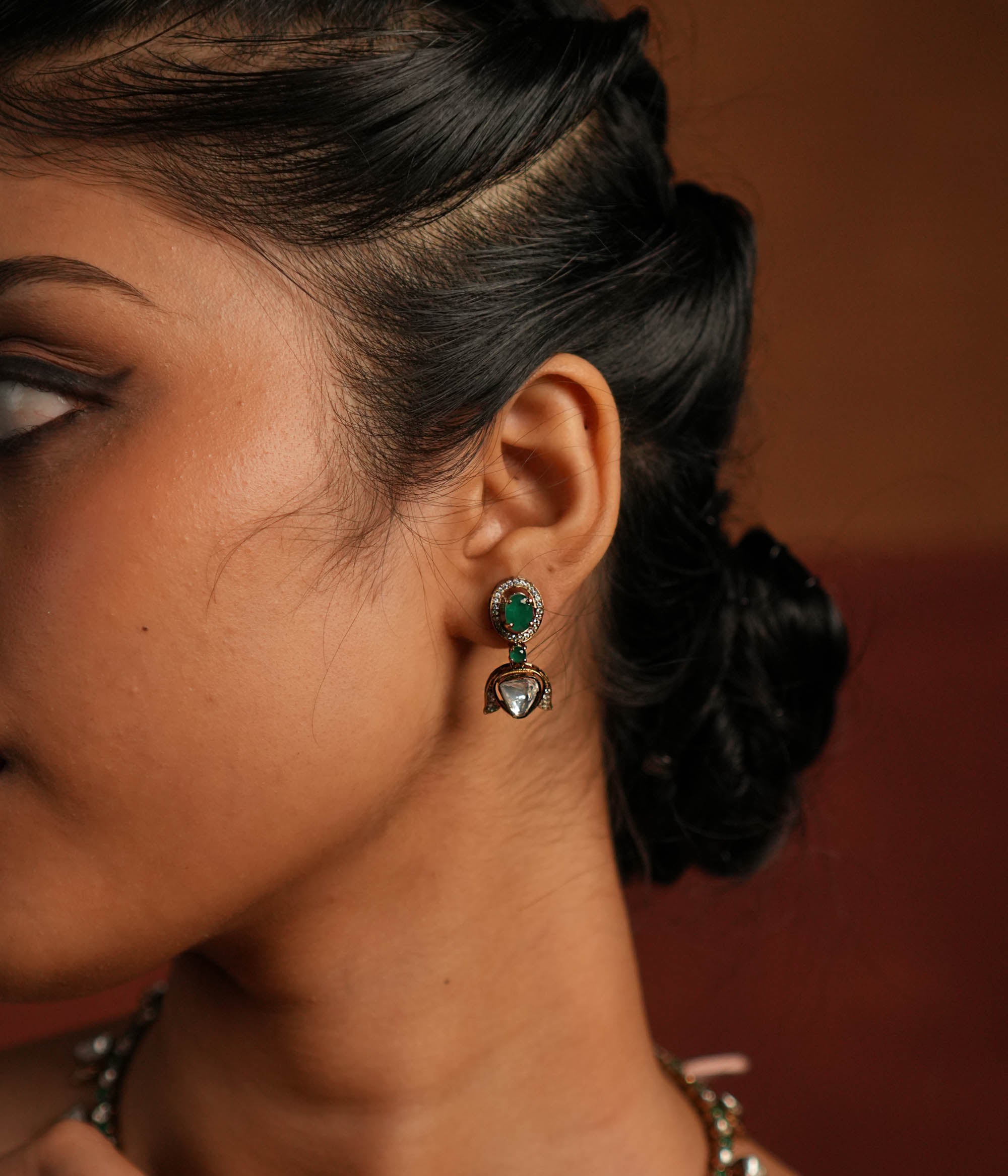 Elegant gold-plated silver drop earrings featuring a striking green spinel stone at the center, beautifully encased by shimmering CZ stones. The design is enhanced with a delicate Polki stone drop, also surrounded by CZ stones, adding a touch of timeless charm. A perfect blend of sophistication and elegance, making it an exquisite statement accessory.