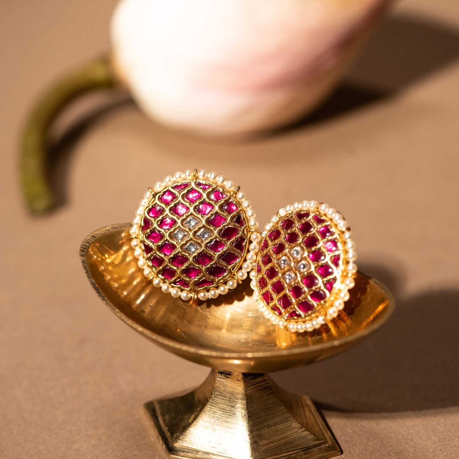 Gold-plated silver round stud earrings featuring a traditional design, adorned with red and white Kundan stones at the center, beautifully surrounded by delicate pearls, adding a timeless and elegant touch.