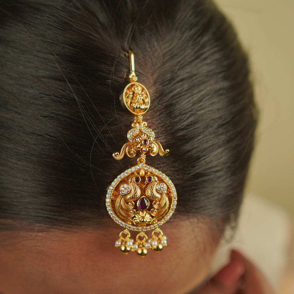Anya Maangtika: A mini heirloom with a modern twist! Crafted in gold-plated silver, this piece features a peacock motif adorned with red spinel stones, CZ stones, and pearls. A perfect blend of classic temple design and delicate elegance for your trousseau.