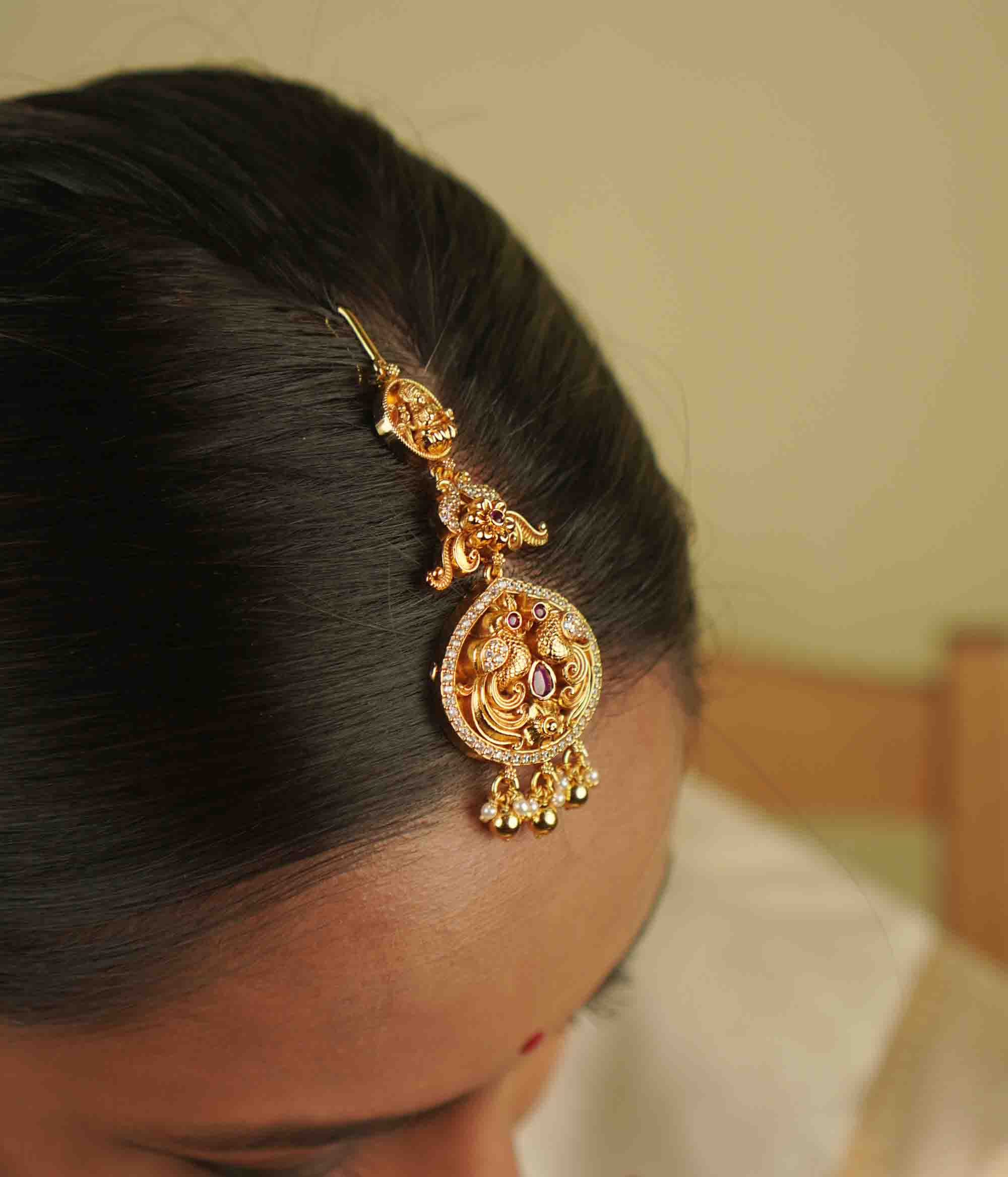 Anya Maangtika: A mini heirloom with a modern twist! Crafted in gold-plated silver, this piece features a peacock motif adorned with red spinel stones, CZ stones, and pearls. A perfect blend of classic temple design and delicate elegance for your trousseau.