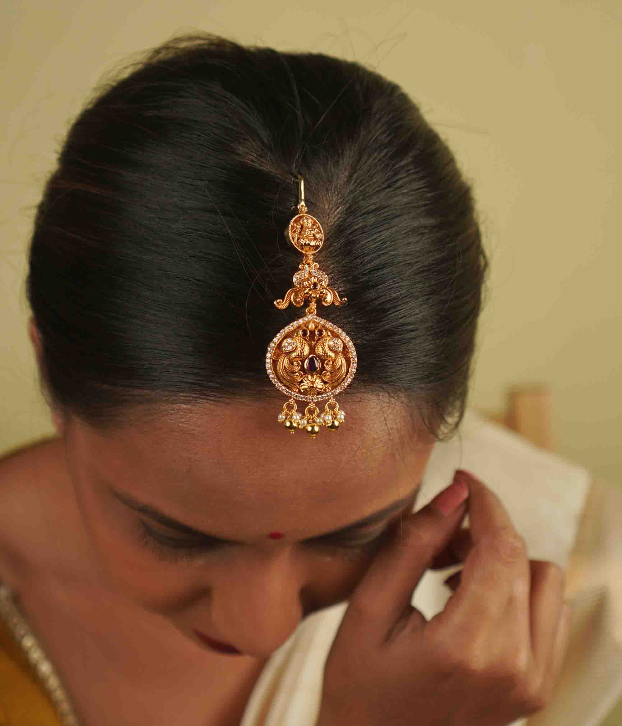 Anya Maangtika: A mini heirloom with a modern twist! Crafted in gold-plated silver, this piece features a peacock motif adorned with red spinel stones, CZ stones, and pearls. A perfect blend of classic temple design and delicate elegance for your trousseau.