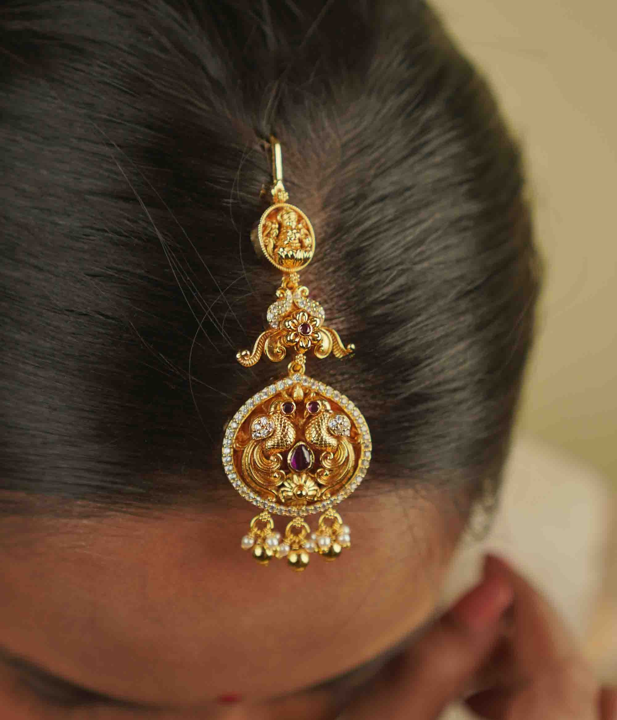 Anya Maangtika: A mini heirloom with a modern twist! Crafted in gold-plated silver, this piece features a peacock motif adorned with red spinel stones, CZ stones, and pearls. A perfect blend of classic temple design and delicate elegance for your trousseau.