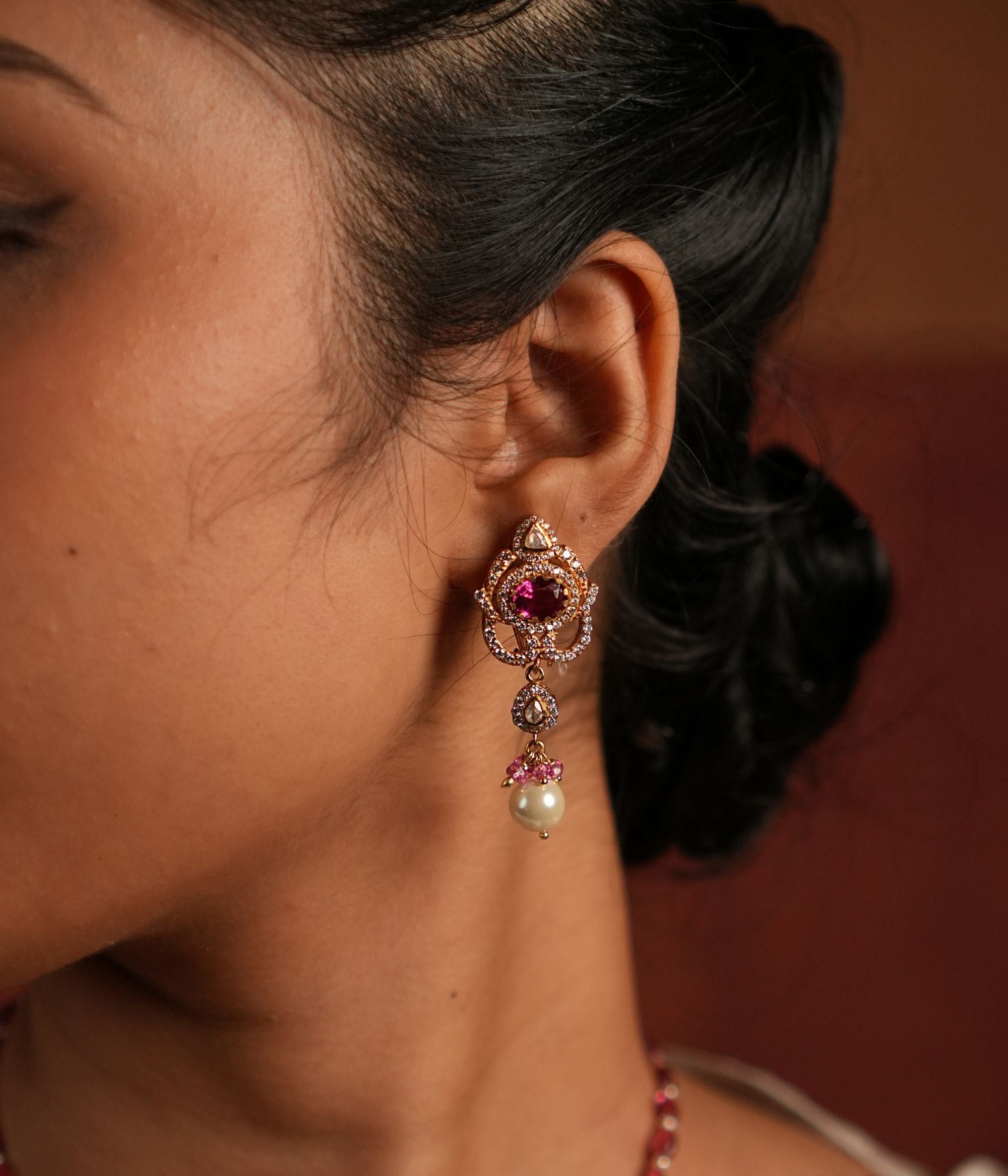 A dazzling gold-plated silver drop earring featuring a captivating Rose Quartz stone at the center, elegantly surrounded by shimmering CZ stones. The graceful drop showcases a radiant Polki stone, complemented by a delicate white pearl and soft pink beads, adding a touch of sophistication and charm. Perfect for an elegant and timeless look.