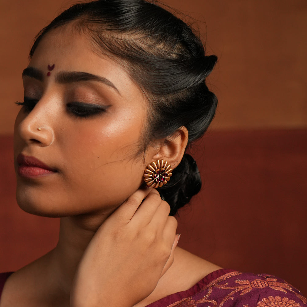 These gold-plated silver stud earrings exude a bold tribal charm with a touch of elegance. Encircled by striking spikes, the fiery red gemstone floral centerpiece reflects the wild beauty of Kolhapuri heritage, making it a statement piece with timeless appeal.