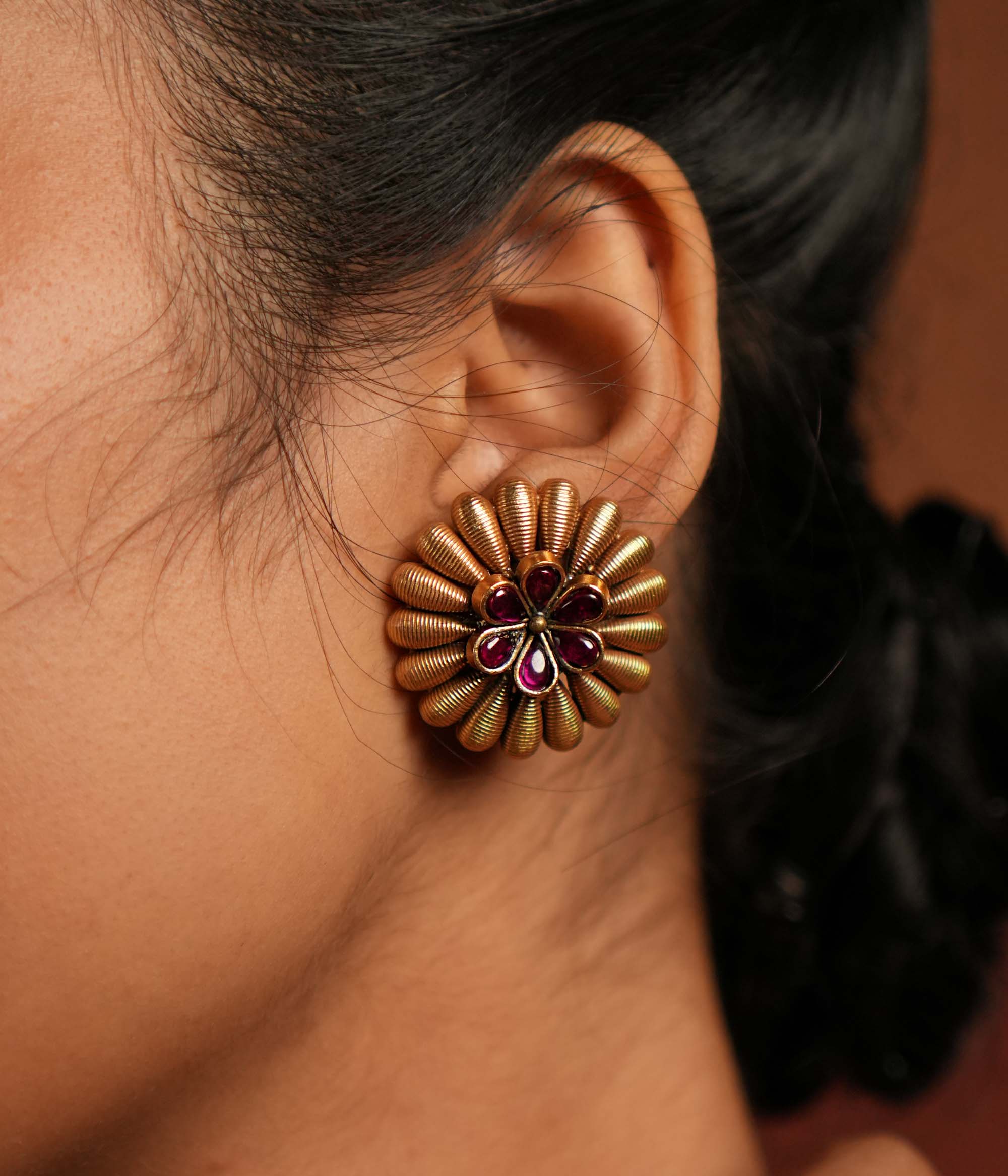 These gold-plated silver stud earrings exude a bold tribal charm with a touch of elegance. Encircled by striking spikes, the fiery red gemstone floral centerpiece reflects the wild beauty of Kolhapuri heritage, making it a statement piece with timeless appeal.