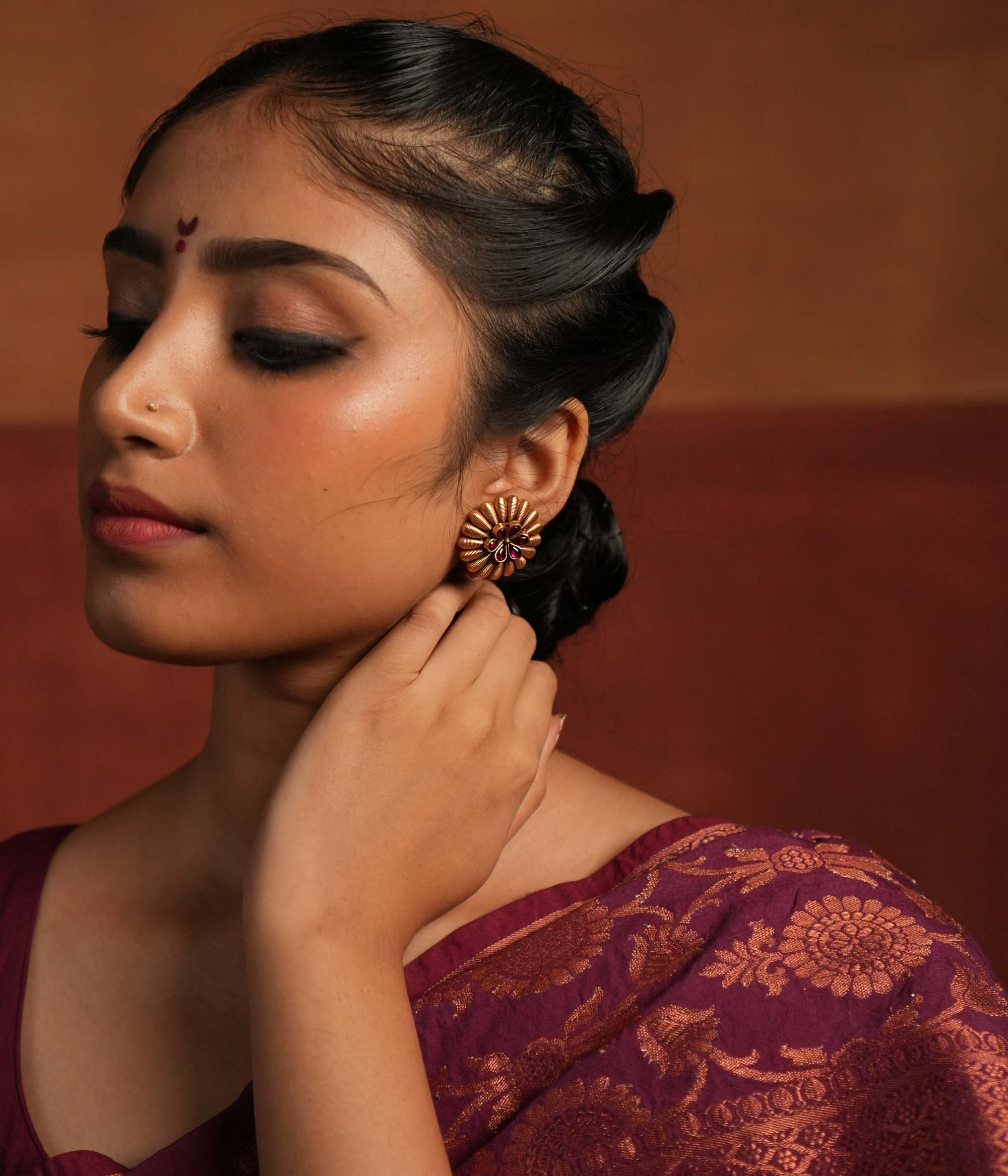 These gold-plated silver stud earrings exude a bold tribal charm with a touch of elegance. Encircled by striking spikes, the fiery red gemstone floral centerpiece reflects the wild beauty of Kolhapuri heritage, making it a statement piece with timeless appeal.