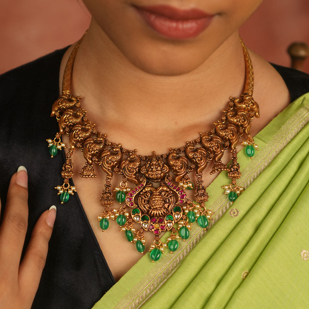 Temple whispers reborn! Antique gold-plated necklace adorned with goddess motifs, kundan stones, pearls, and green beads, echoing divine elegance and timeless heritage.