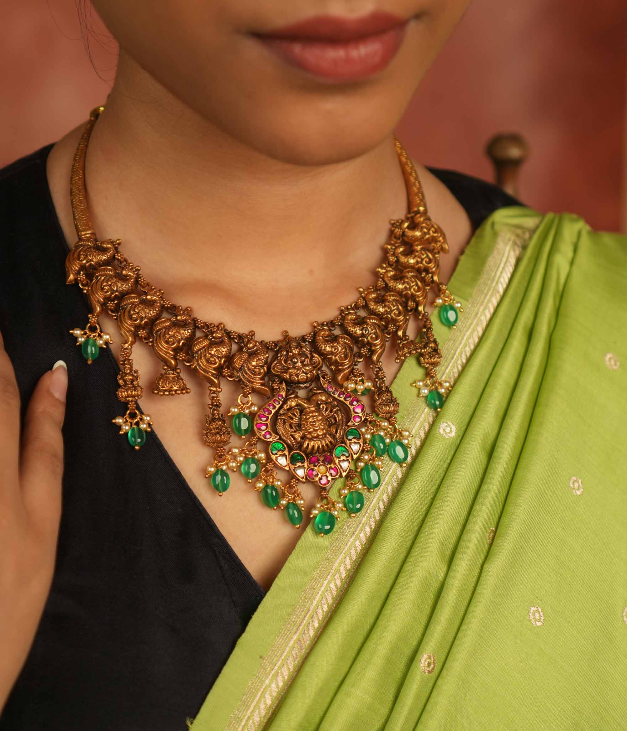 Temple whispers reborn! Antique gold-plated necklace adorned with goddess motifs, kundan stones, pearls, and green beads, echoing divine elegance and timeless heritage.