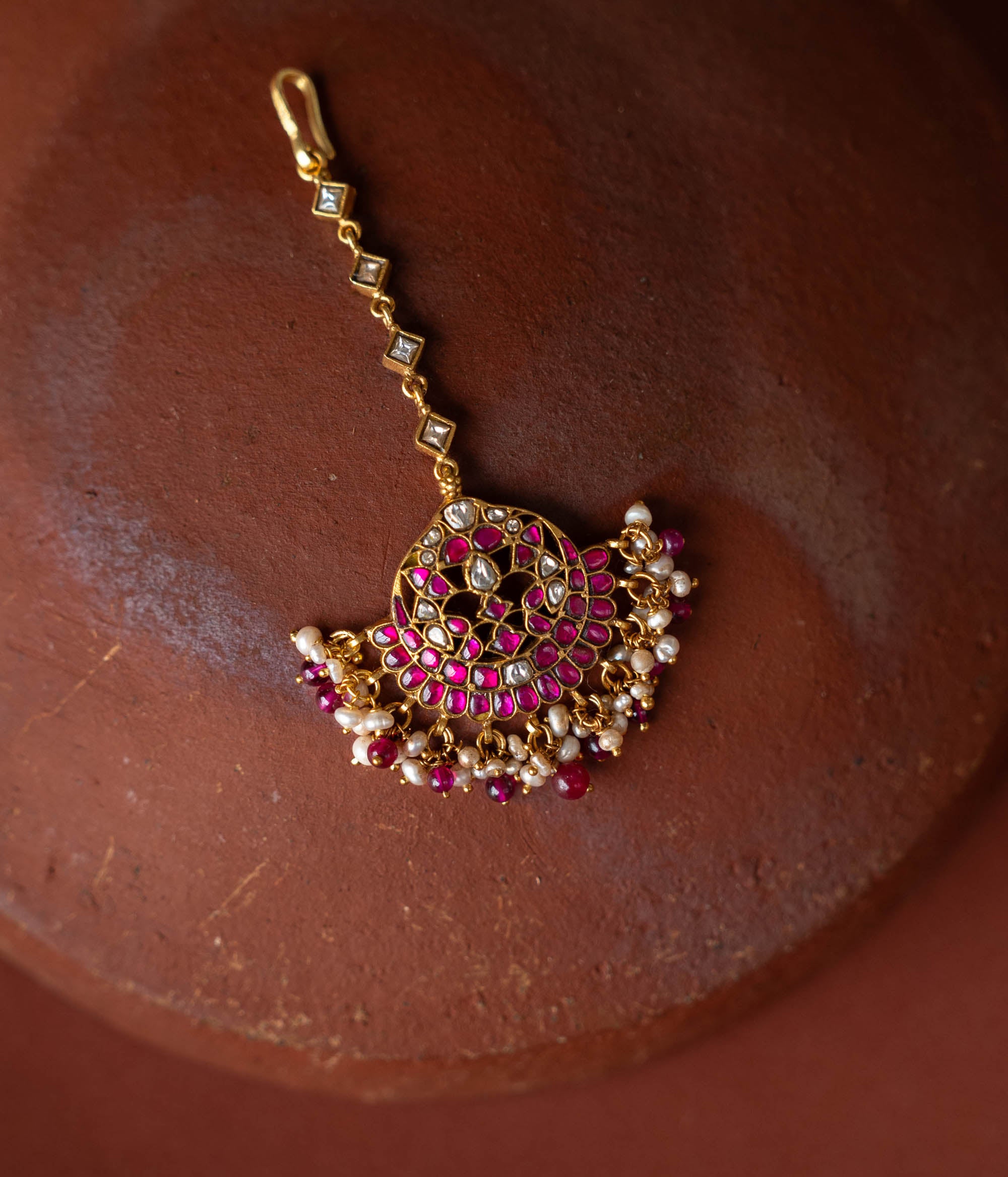 A handcrafted 92.5 sterling silver and 22ct gold-plated Kundan tikka, adorned with red, green, and white Kundan stones, red beads, and pearls, featuring intricate gold detailing and embodying divine grace and timeless elegance.