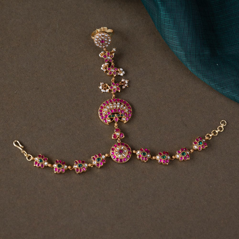 A handcrafted Ruhani Haathphool in 92.5 sterling silver with 22ct gold plating, adorned with white and red Kundan stones and delicate pearls. This exquisite piece features intricate floral motifs, blending celestial charm with regal elegance.