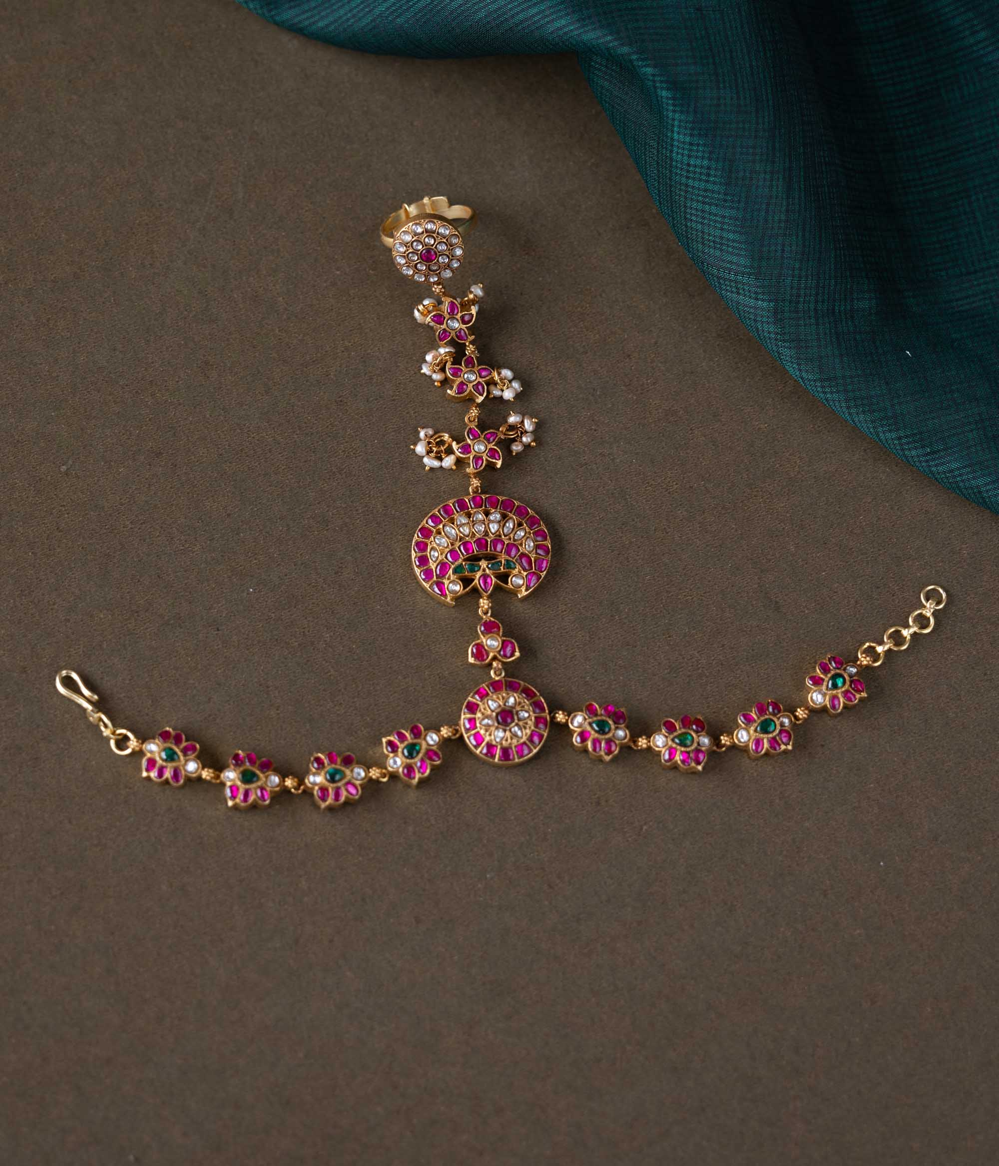 A handcrafted Ruhani Haathphool in 92.5 sterling silver with 22ct gold plating, adorned with white and red Kundan stones and delicate pearls. This exquisite piece features intricate floral motifs, blending celestial charm with regal elegance.