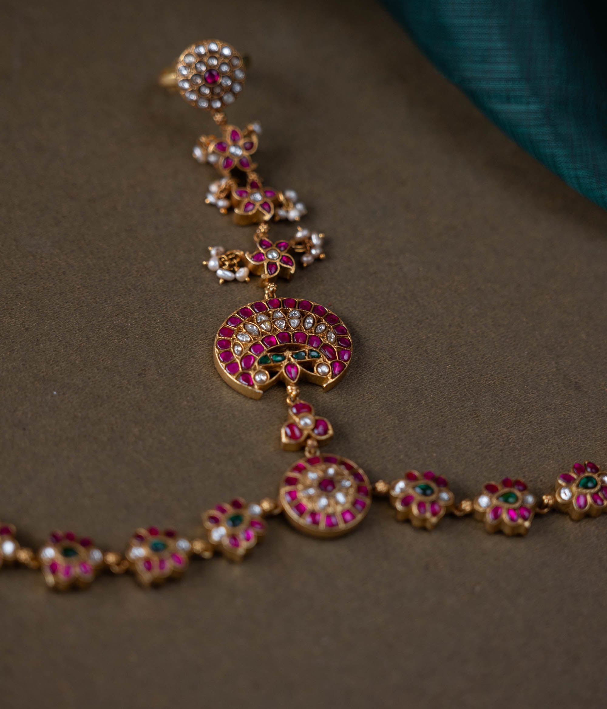 A handcrafted Ruhani Haathphool in 92.5 sterling silver with 22ct gold plating, adorned with white and red Kundan stones and delicate pearls. This exquisite piece features intricate floral motifs, blending celestial charm with regal elegance.