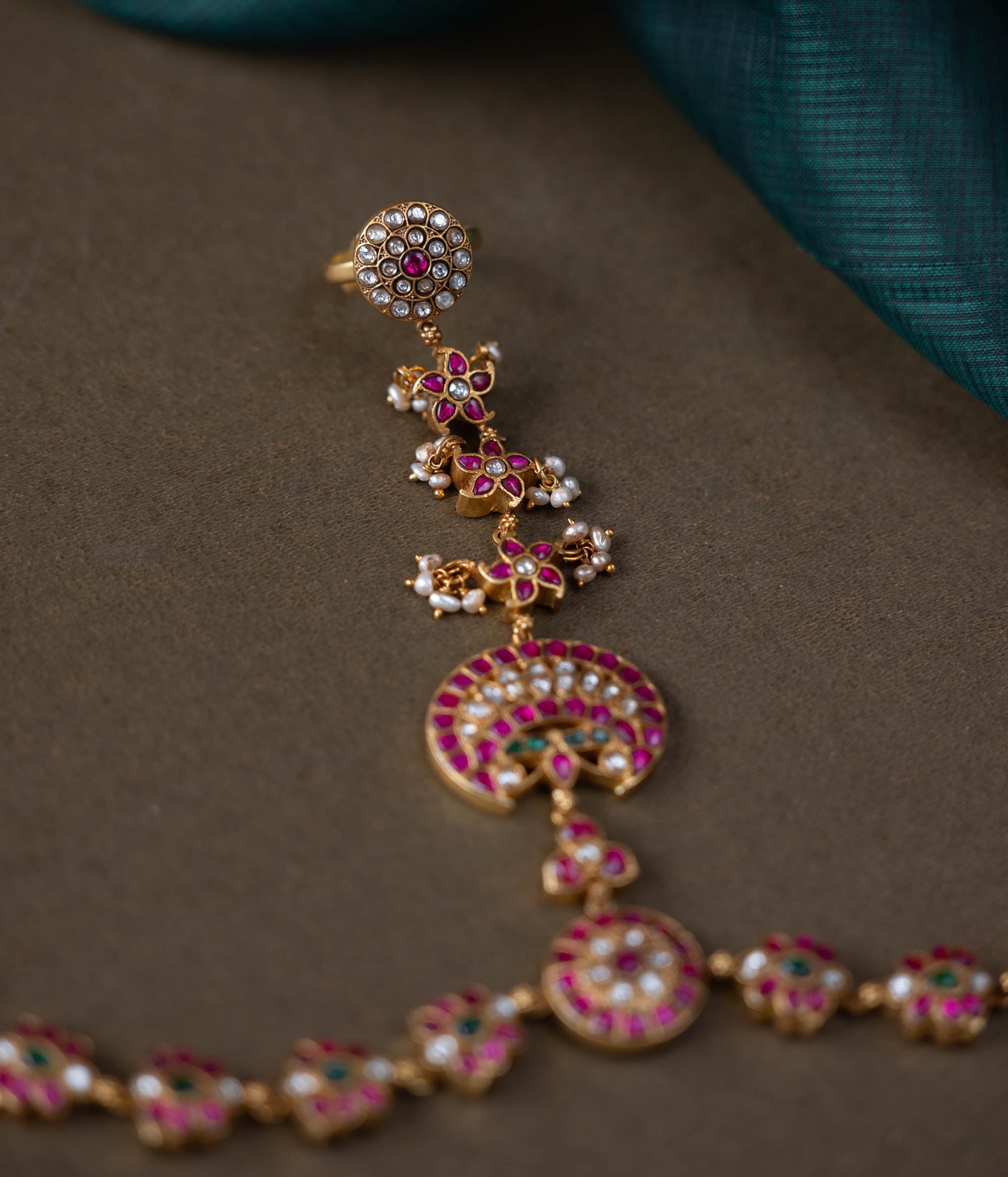 A handcrafted Ruhani Haathphool in 92.5 sterling silver with 22ct gold plating, adorned with white and red Kundan stones and delicate pearls. This exquisite piece features intricate floral motifs, blending celestial charm with regal elegance.