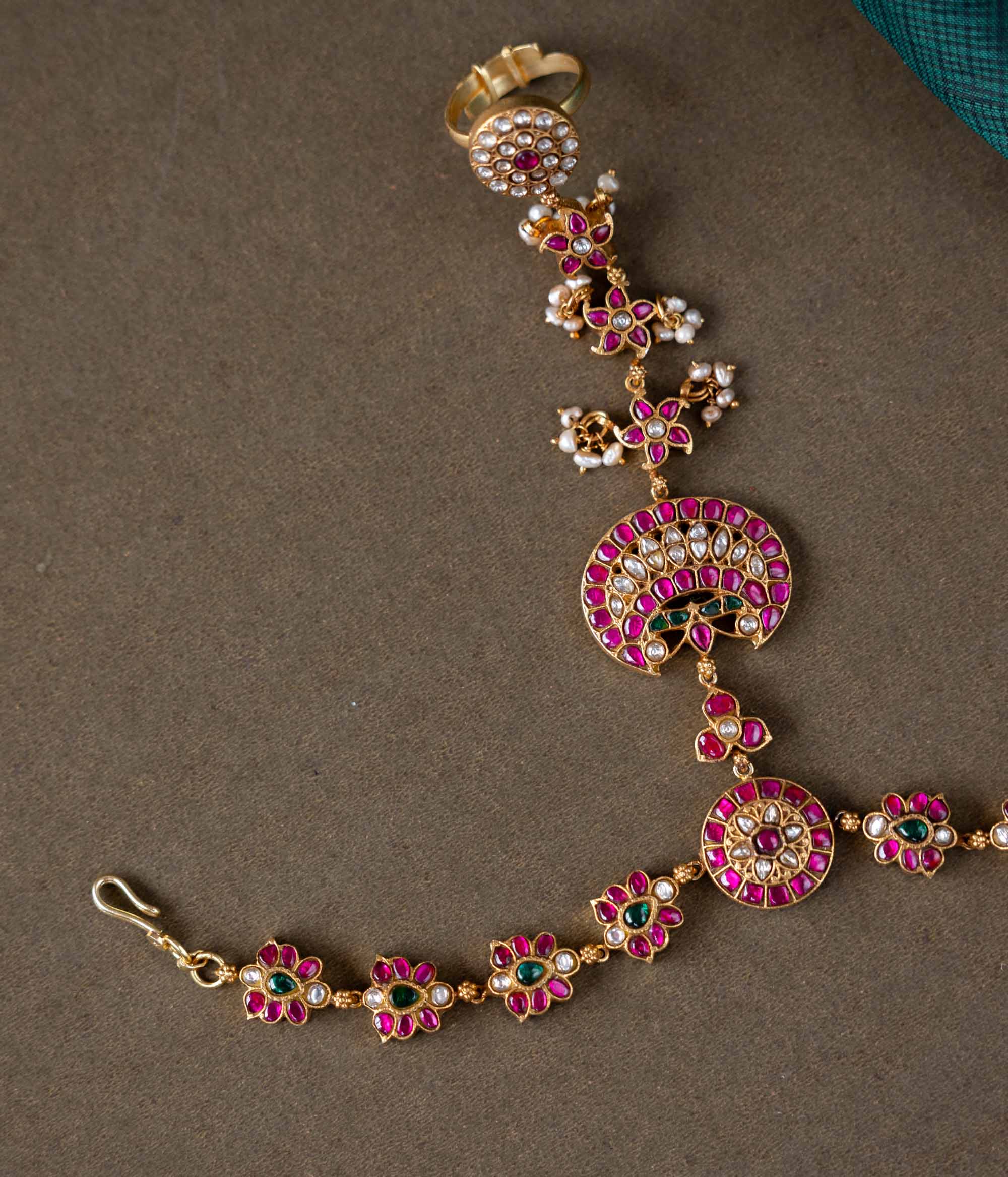 A handcrafted Ruhani Haathphool in 92.5 sterling silver with 22ct gold plating, adorned with white and red Kundan stones and delicate pearls. This exquisite piece features intricate floral motifs, blending celestial charm with regal elegance.