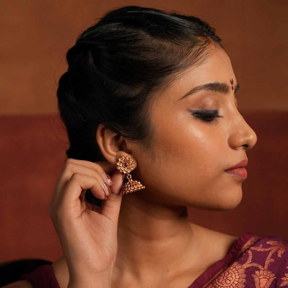 Exquisite jhumka earrings featuring a floral design engraved with intricate tiny floral details. The centerpiece showcases a striking red Kundan stone, enhancing the elegance of the design. The jhumka structure adds a traditional touch, making it a timeless statement piece.
