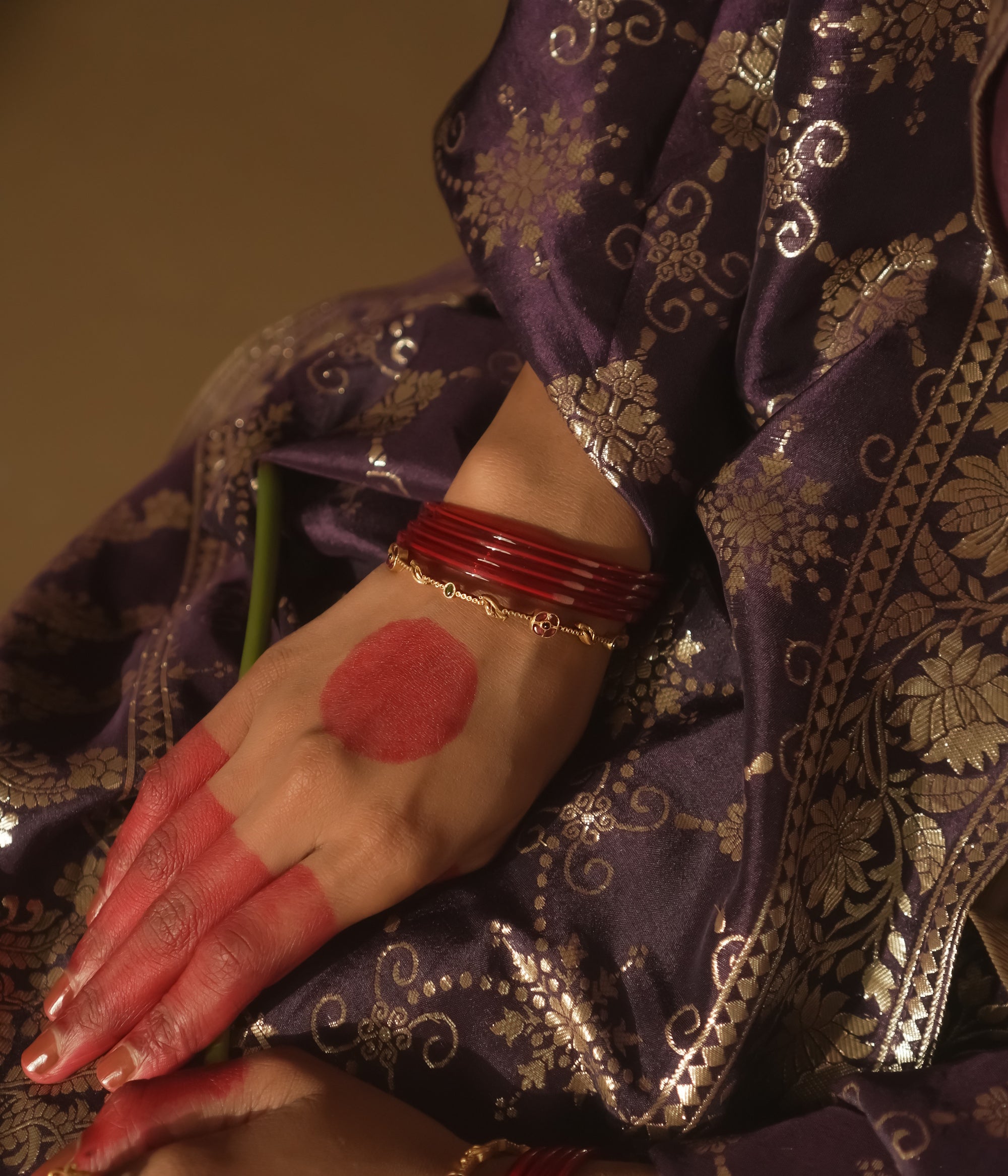 Hand with red polish and gold bangles on a purple fabric background
