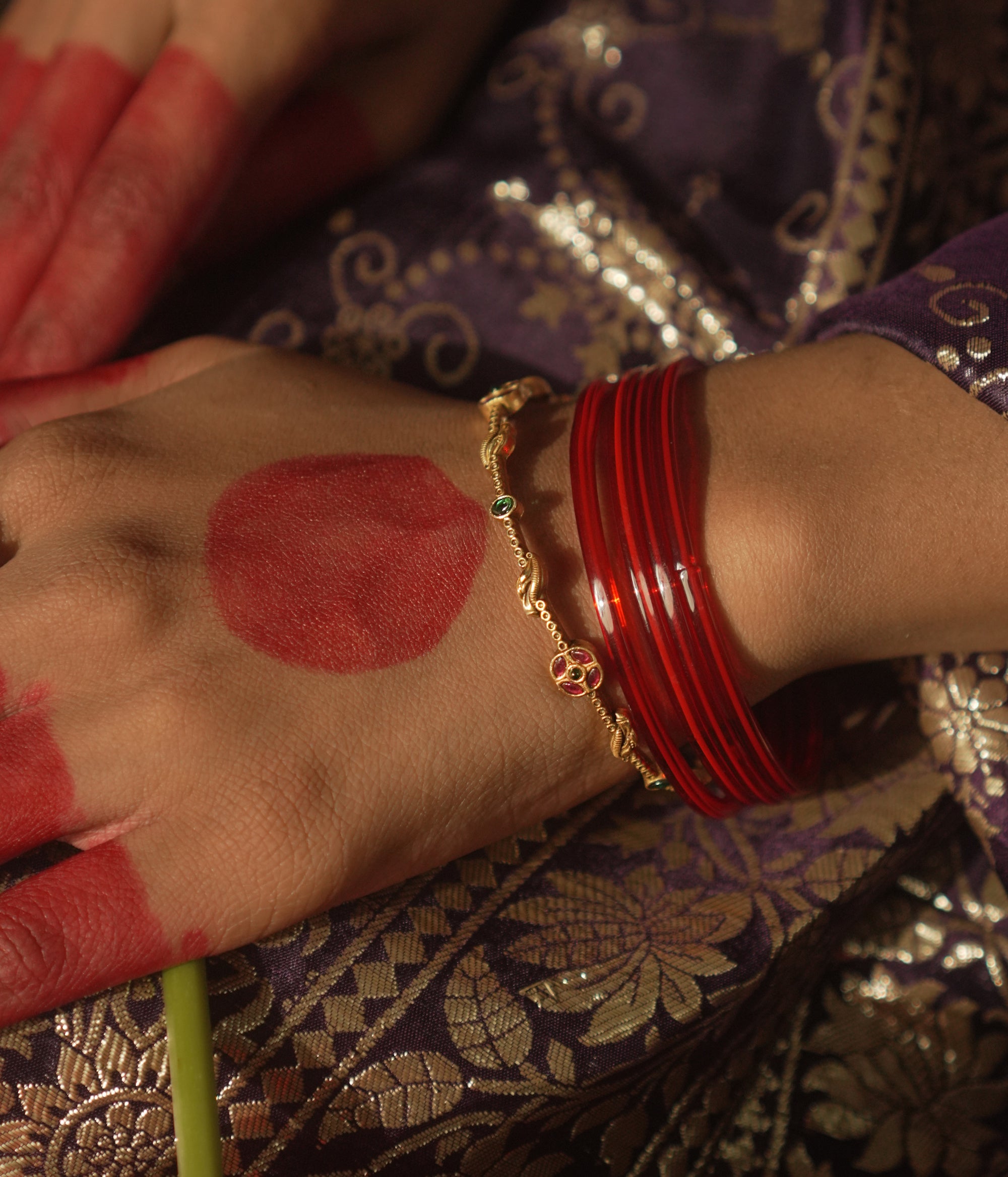 Close-up of a hand with red bangles and gold bracelet on a patterned fabric background