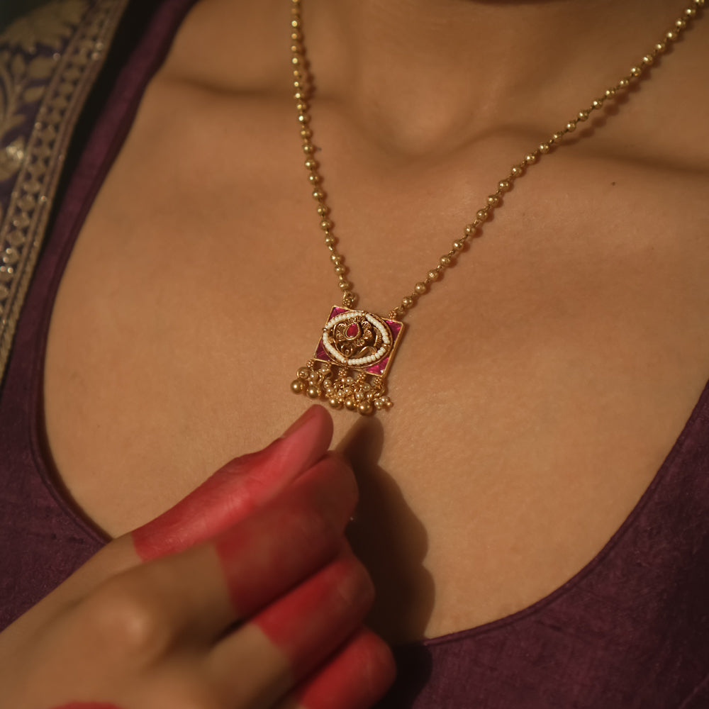 Necklace with gold beads and a square pendant with pink gemstones and gold filigree.