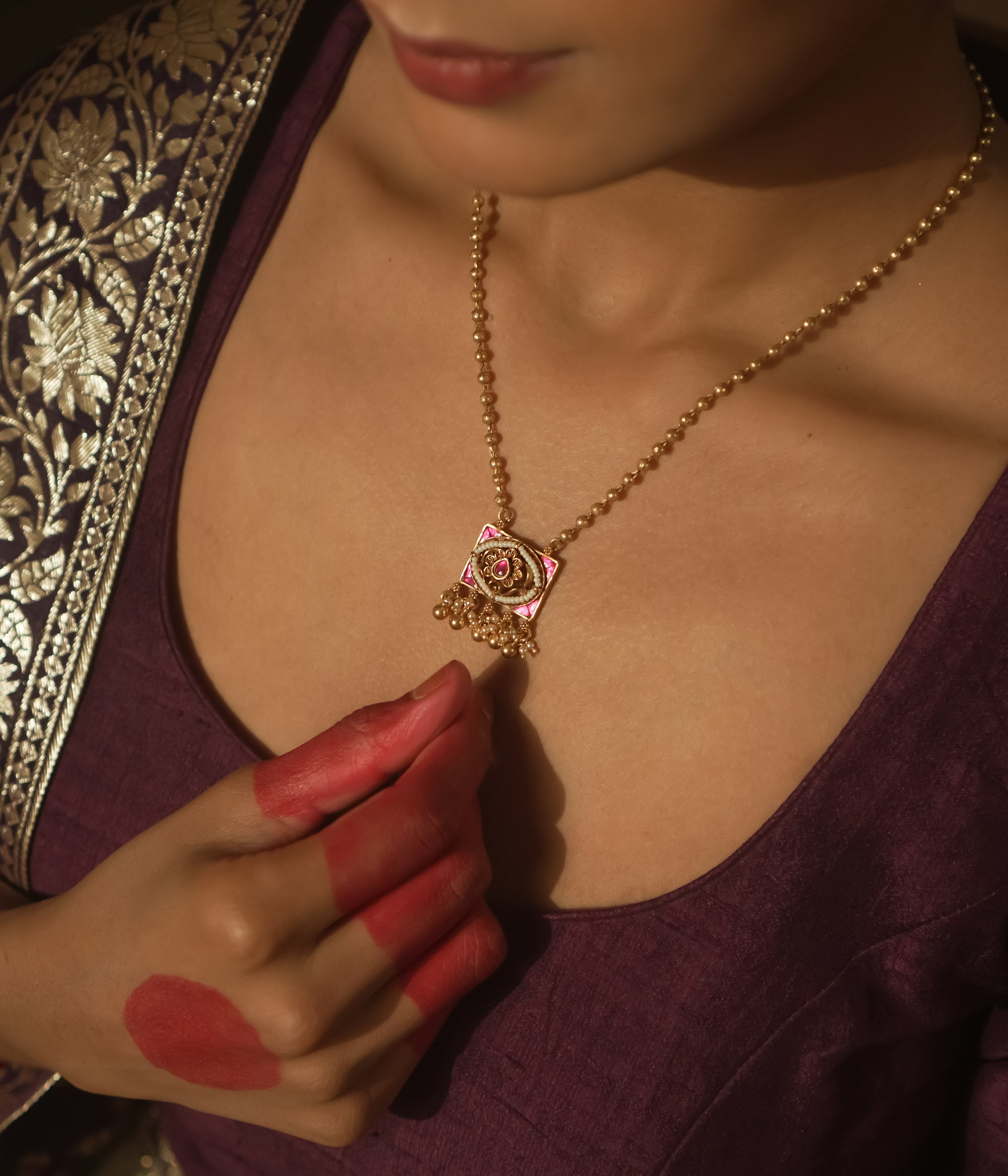Necklace with gold beads and a square pendant with pink gemstones and gold filigree.