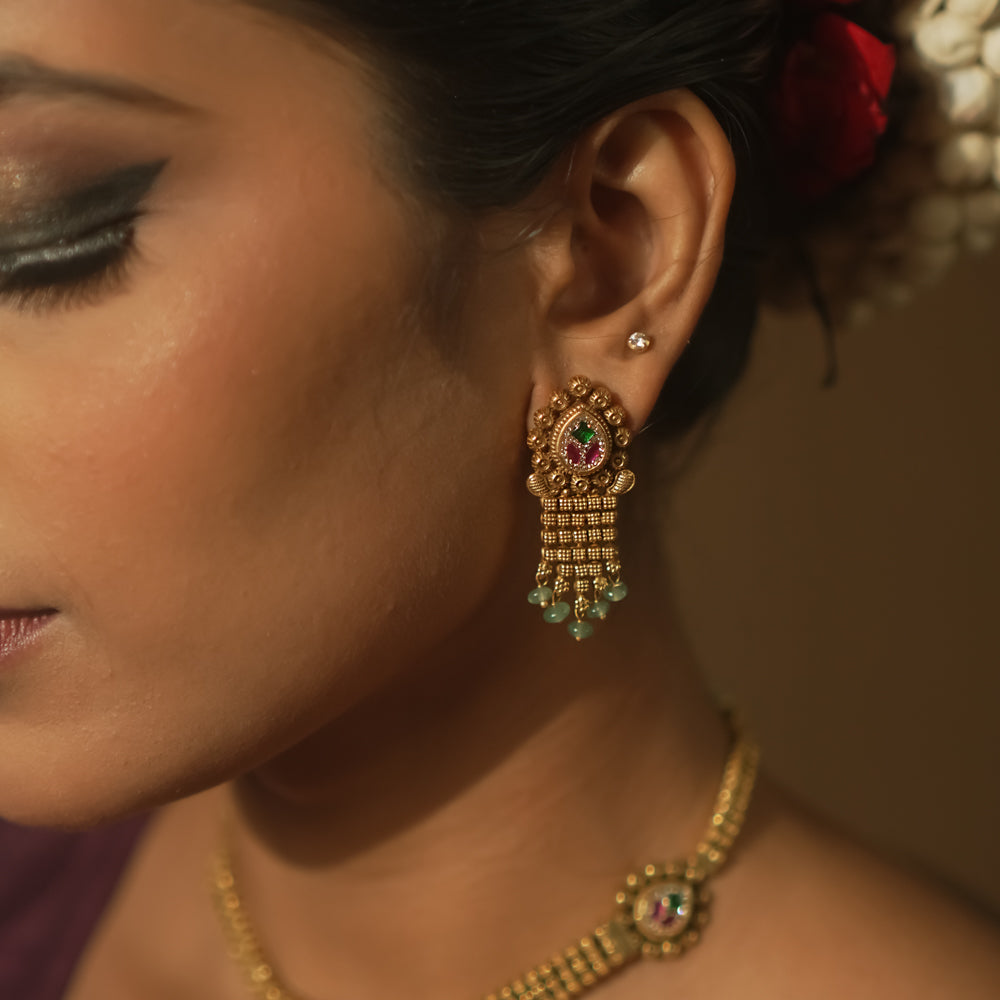 Gold earrings with teardrop charms, vibrant Kundan, and emerald fringes.