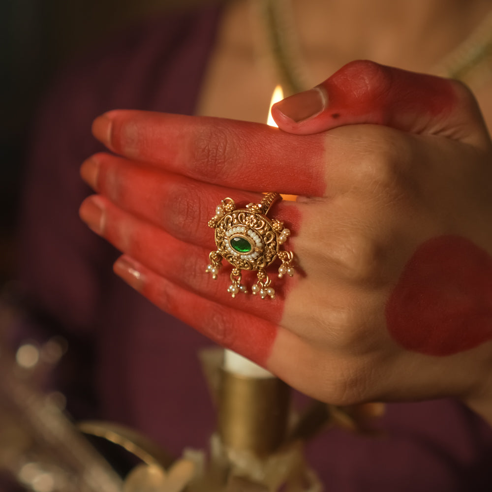 Gold ring with a sun motif, a central emerald Kundan, and filigree petals.