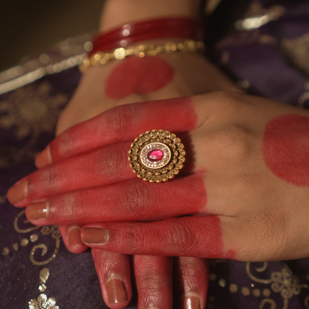 Gold ring with an antique design, tiny gems, and a central crimson jewel.
