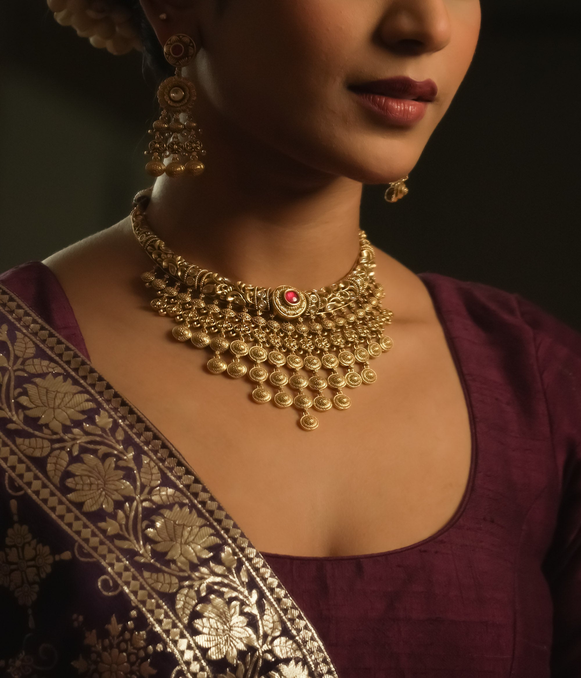 Gold necklace with dangling coin motifs and a central pendant with red gems.