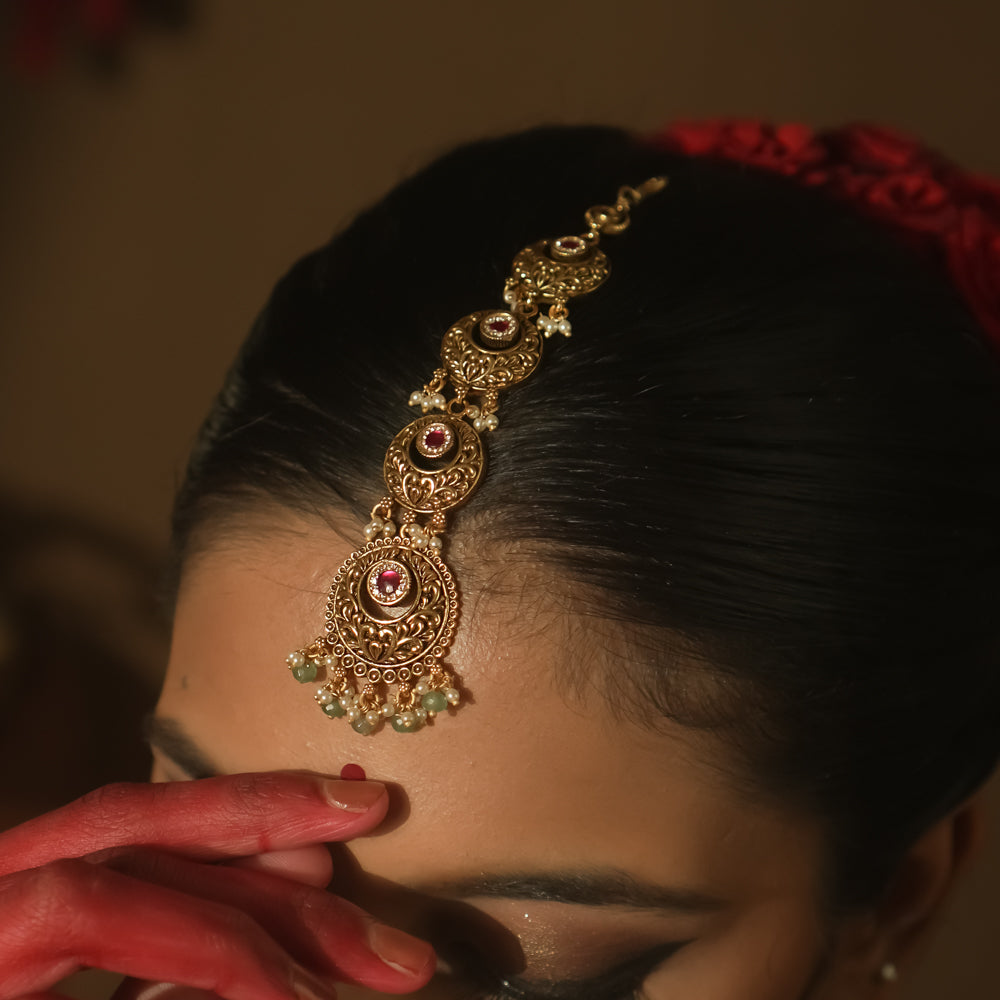 Gold-plated silver maangtika with red and green gemstones and dangling green beads.