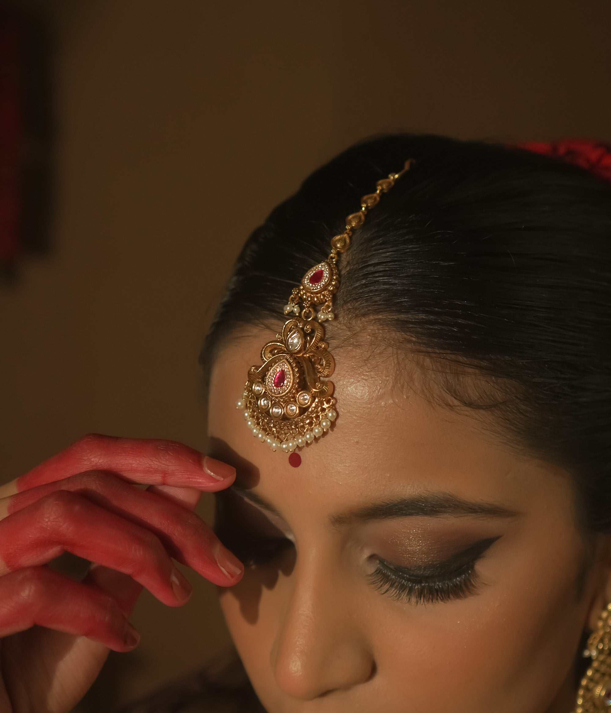 Maangtika with gold swirls, cultured rubies, pearls, and a dangling red gemstone.