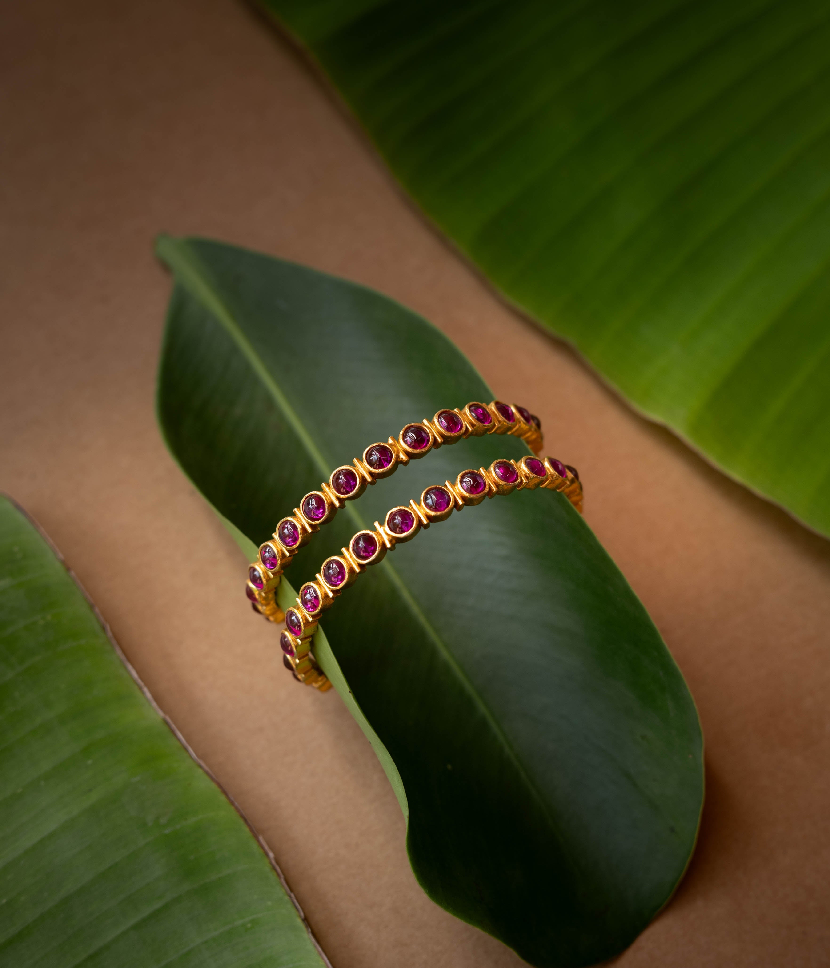 A gold-toned hinged bangle with a row of red stones in the center.