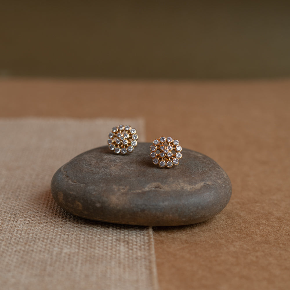 Gold floral stud earrings set with clear Swarovski stones, on a rock surface.