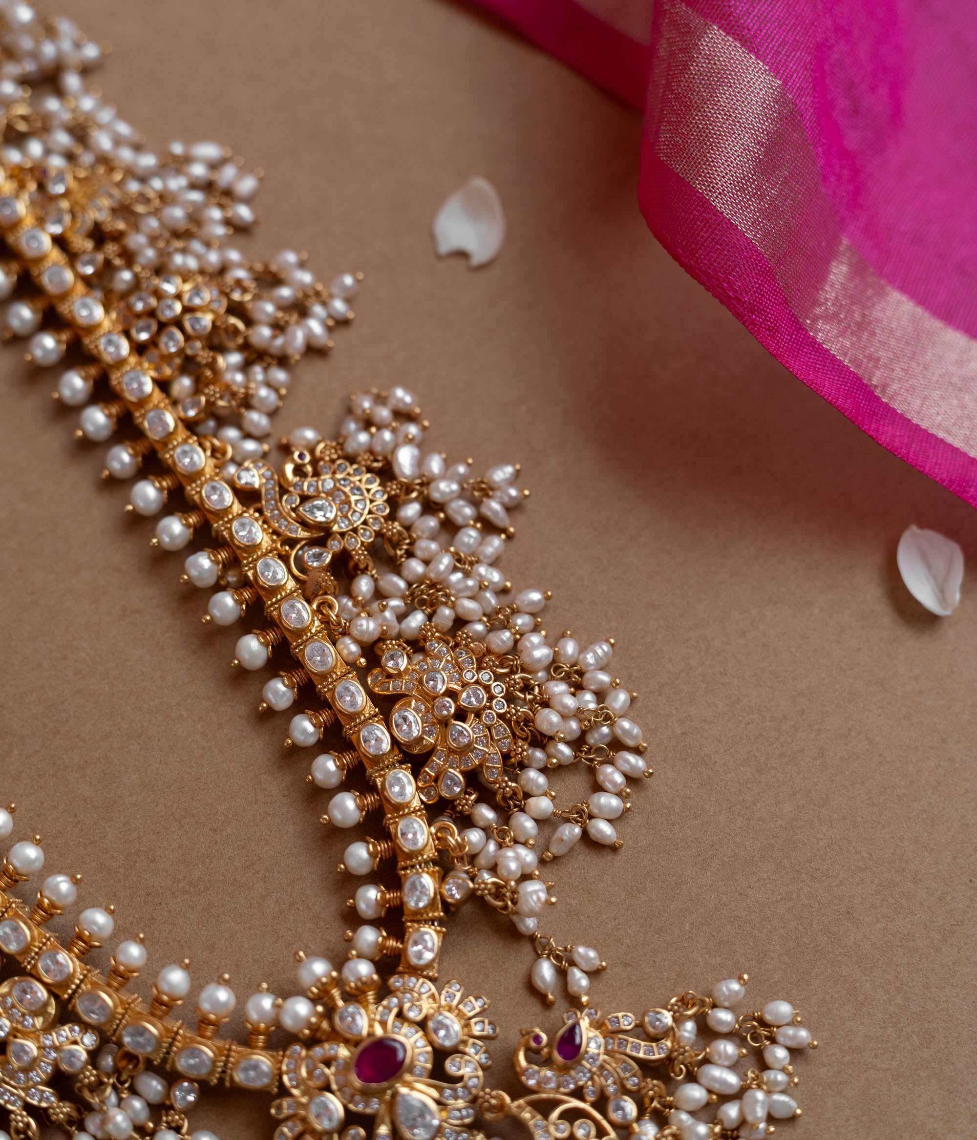 A long gold necklace adorned with numerous small pearls. It features a central pendant with clear and red stones.