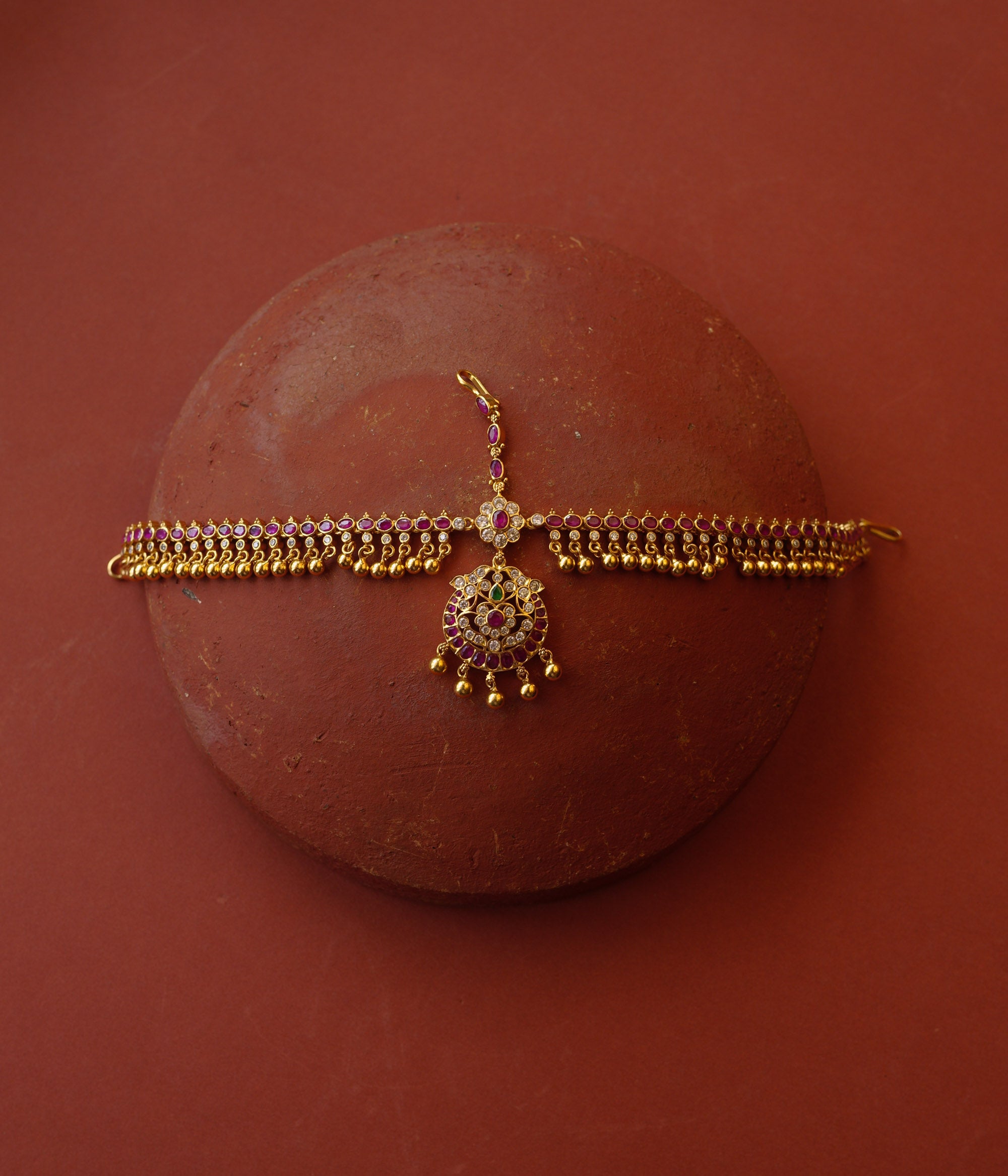 Traditional gold mathapatti with red, green, and Swarovski stones featuring temple bell-like danglers.