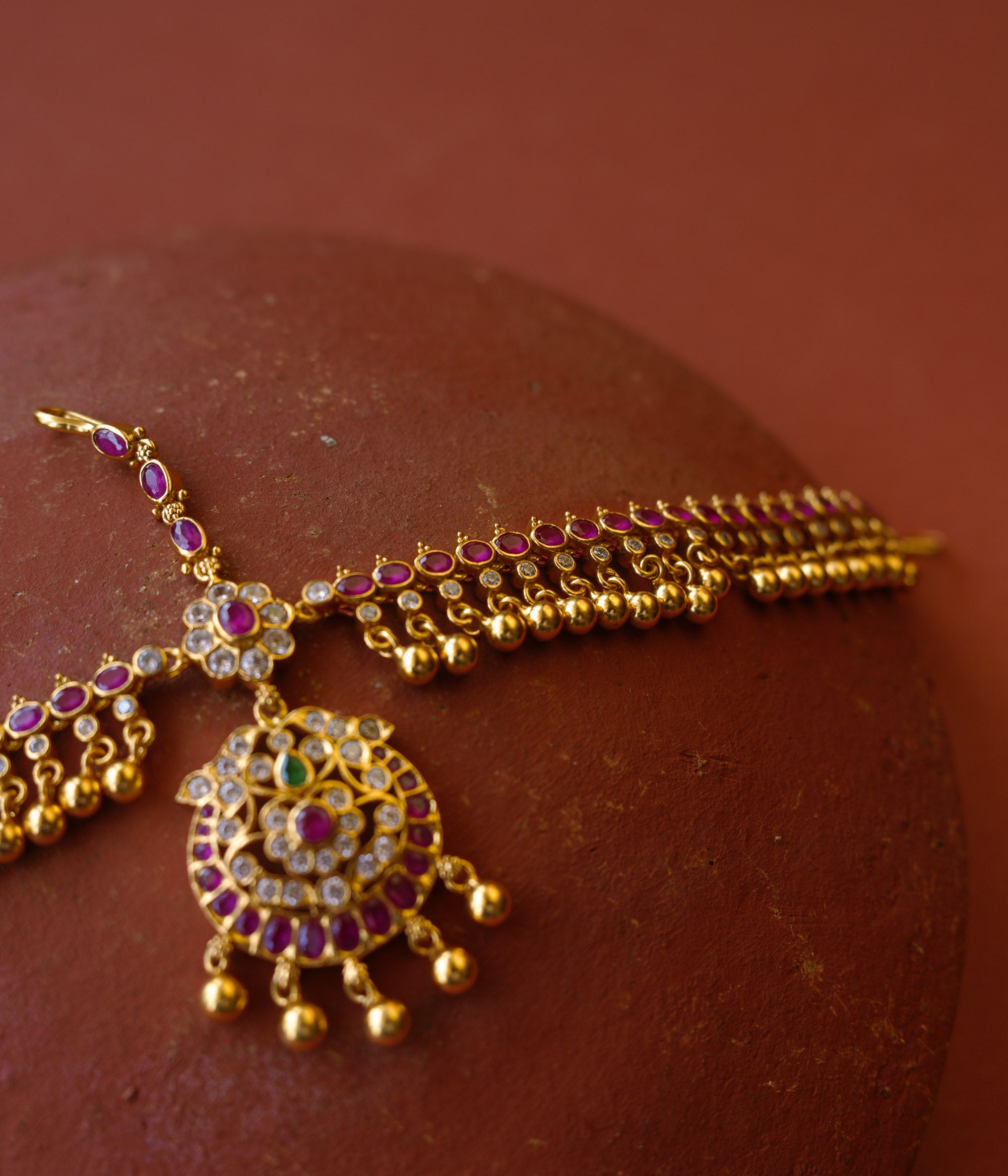 Traditional gold mathapatti with red, green, and Swarovski stones featuring temple bell-like danglers.