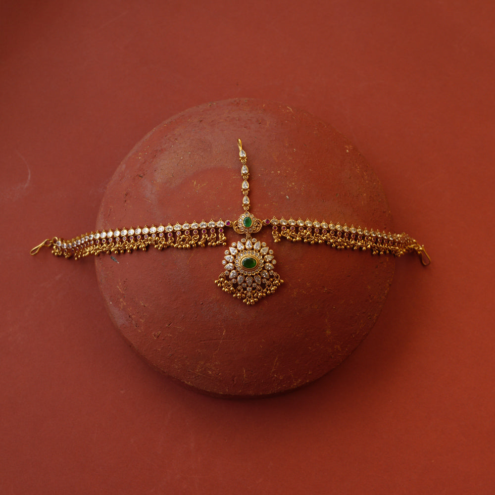 Traditional gold mathapatti with green spinal stone and Swarovski crystals in peacock eye-shaped central design.